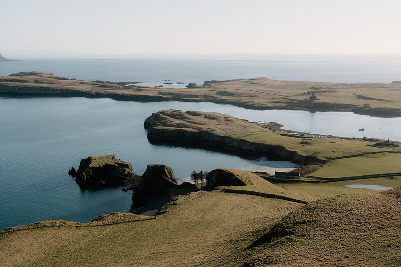 Grassy headlands enclose a calm harbour on the Isle of Canna, tiny figures visible on the rocks below.