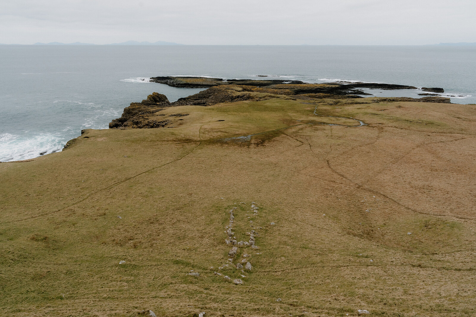 A grassy headland path leads toward rocky skerries on the Isle of Canna's coast.