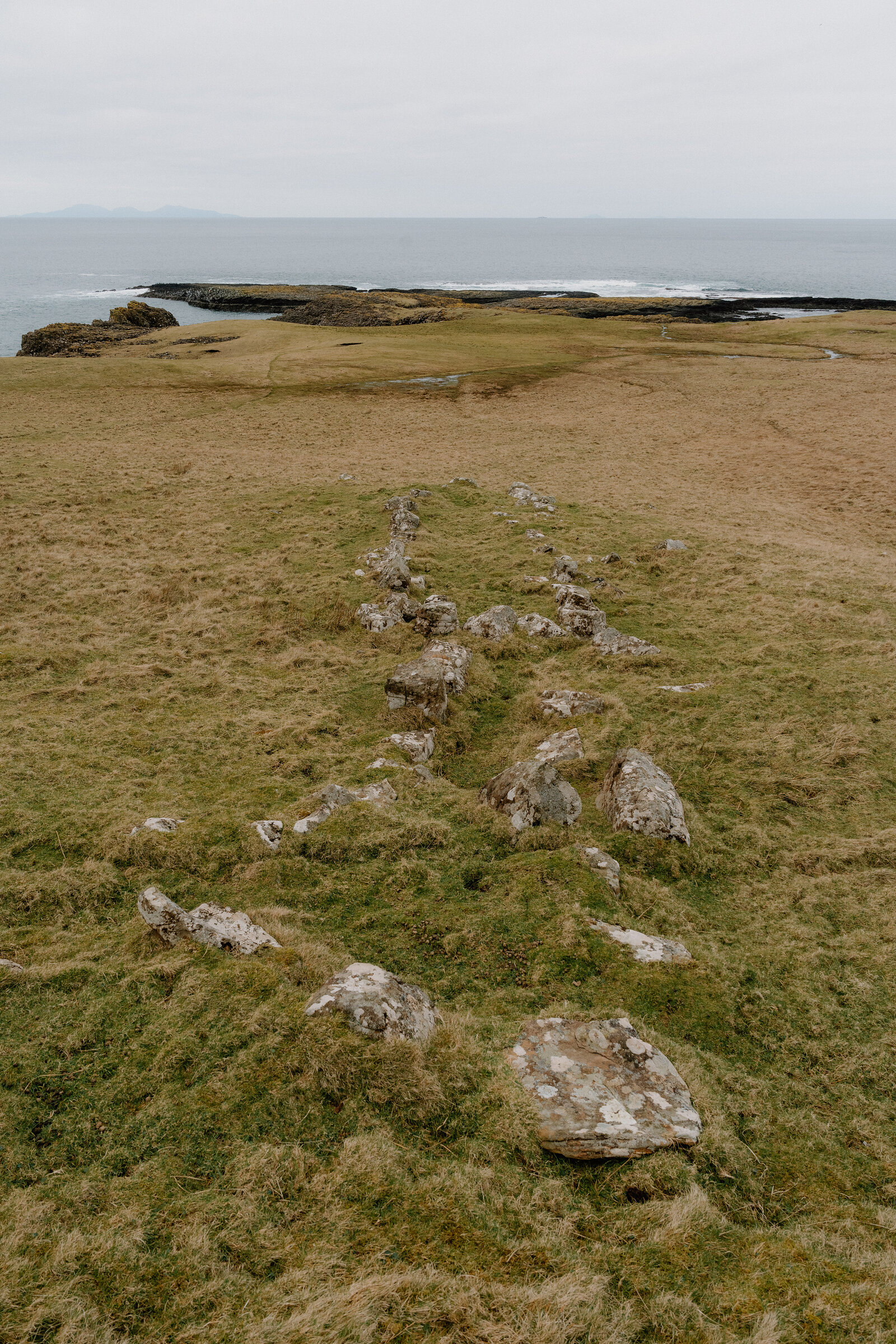A low stone wall's foundation traces a line across a grassy headland on the Isle of Canna.