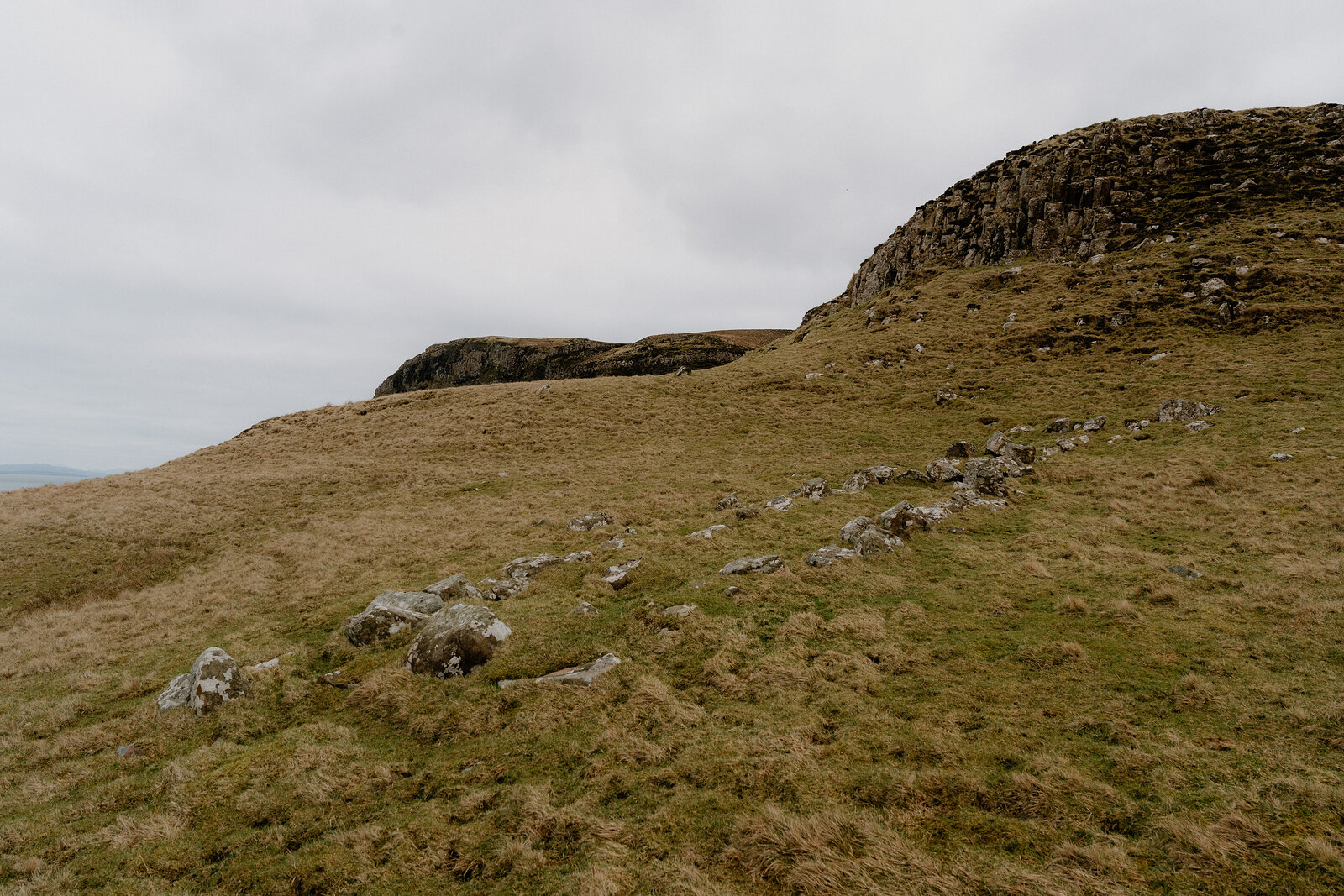 A ruined dry stone wall climbs a grassy slope toward a circular stone structure on the Isle of Canna.