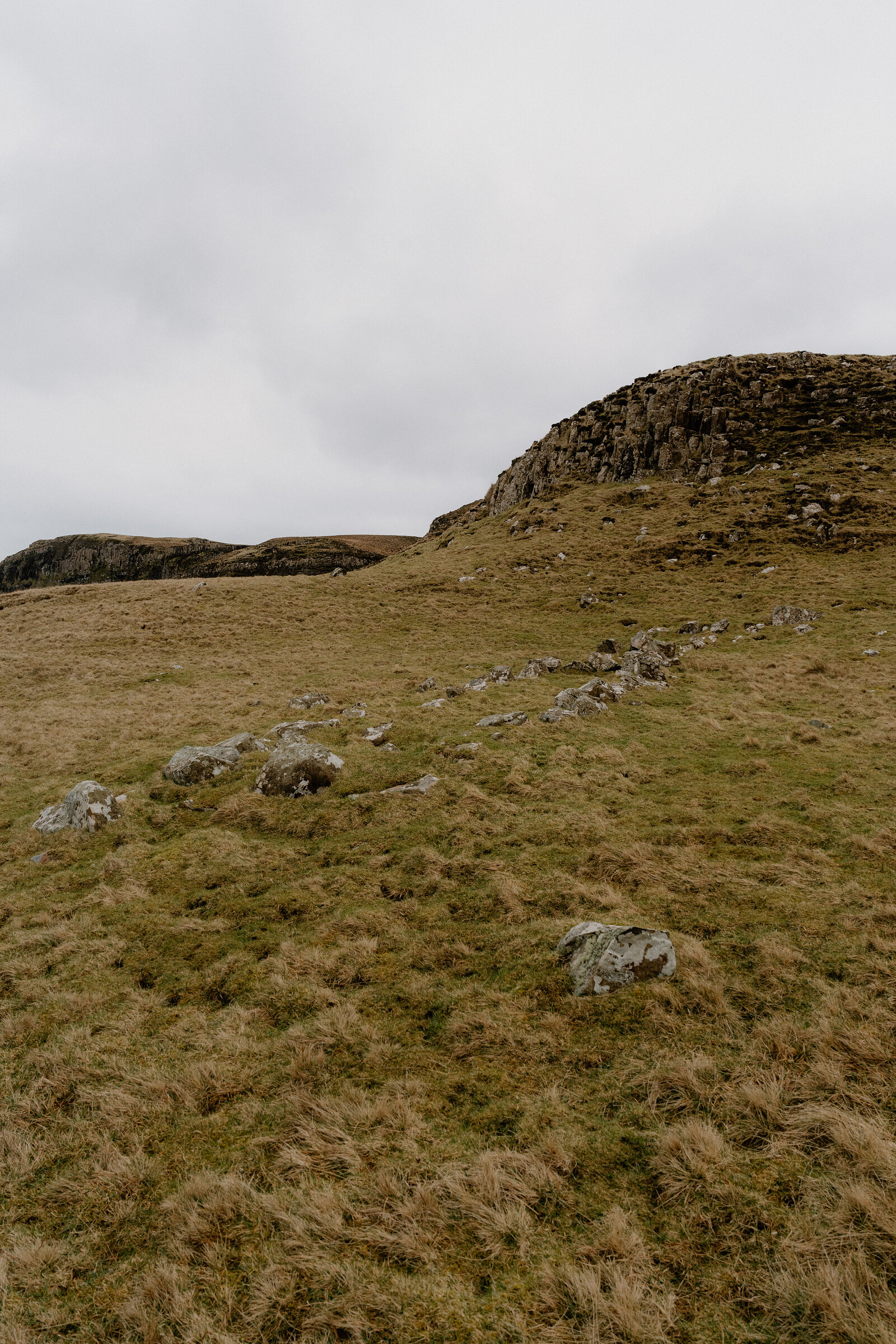 A crumbling stone wall leads up to a round dry stone structure on a grassy Isle of Canna hillside.