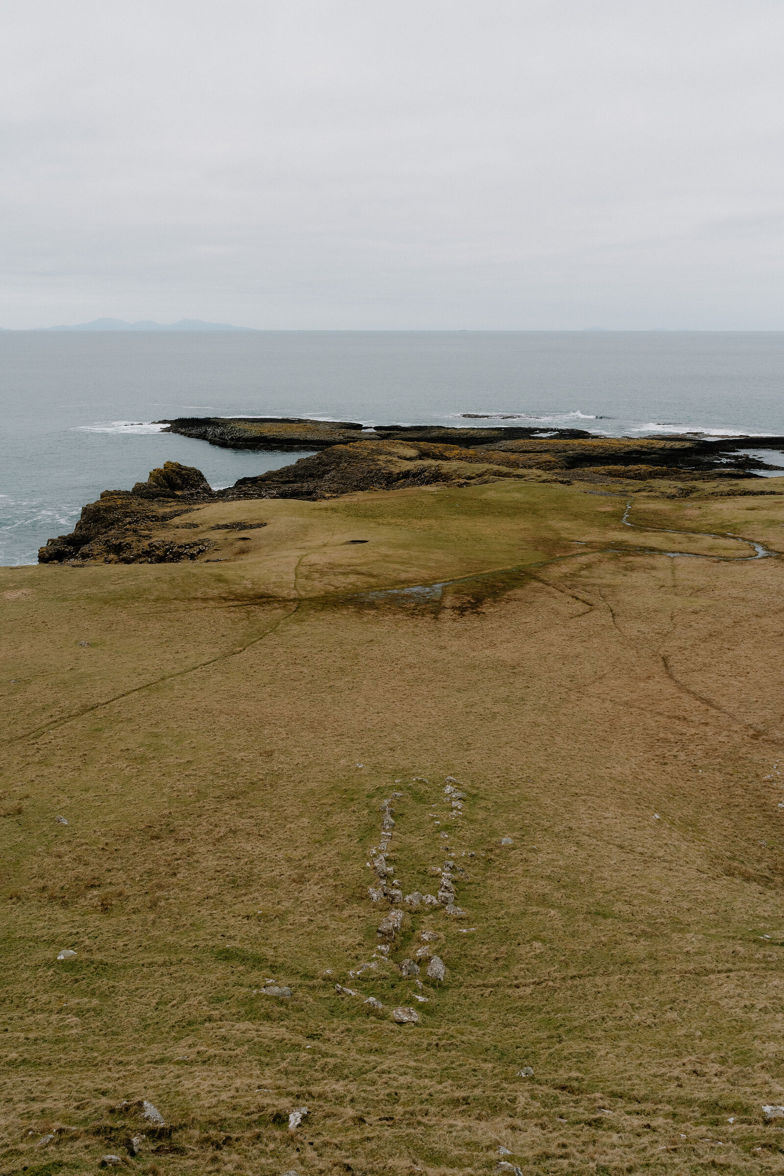 A grassy headland stretches toward rocky skerries and open sea on the Isle of Canna.