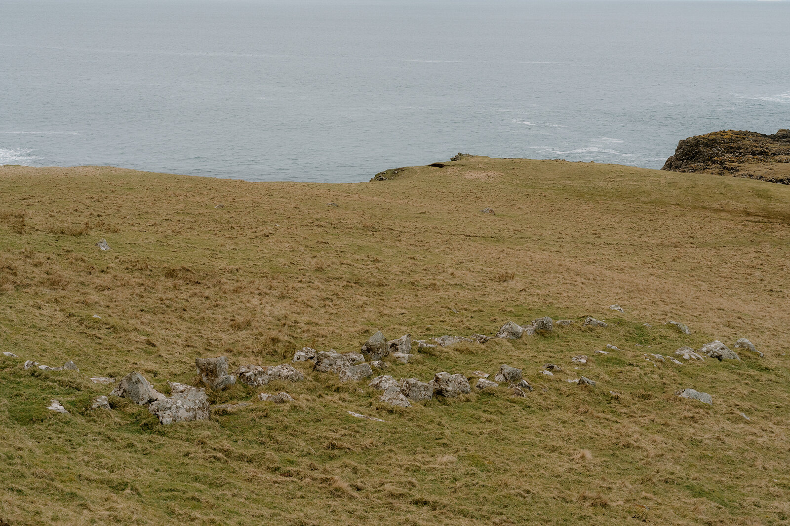 Grassy cliffs curve above a rocky bay on the Isle of Canna's coast.