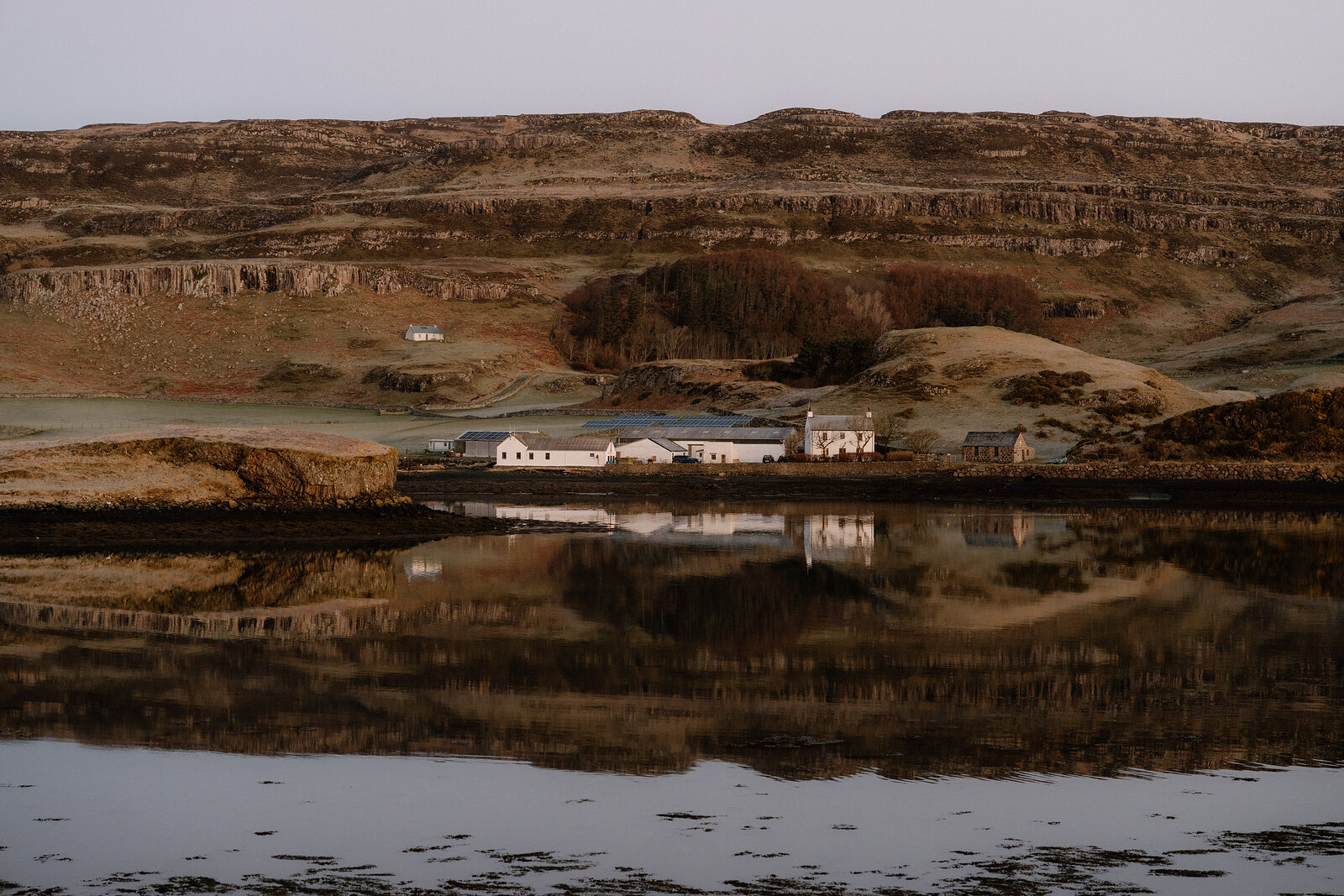 Canna's harbour cottages and their reflections in still water, under the island's terraced hills.