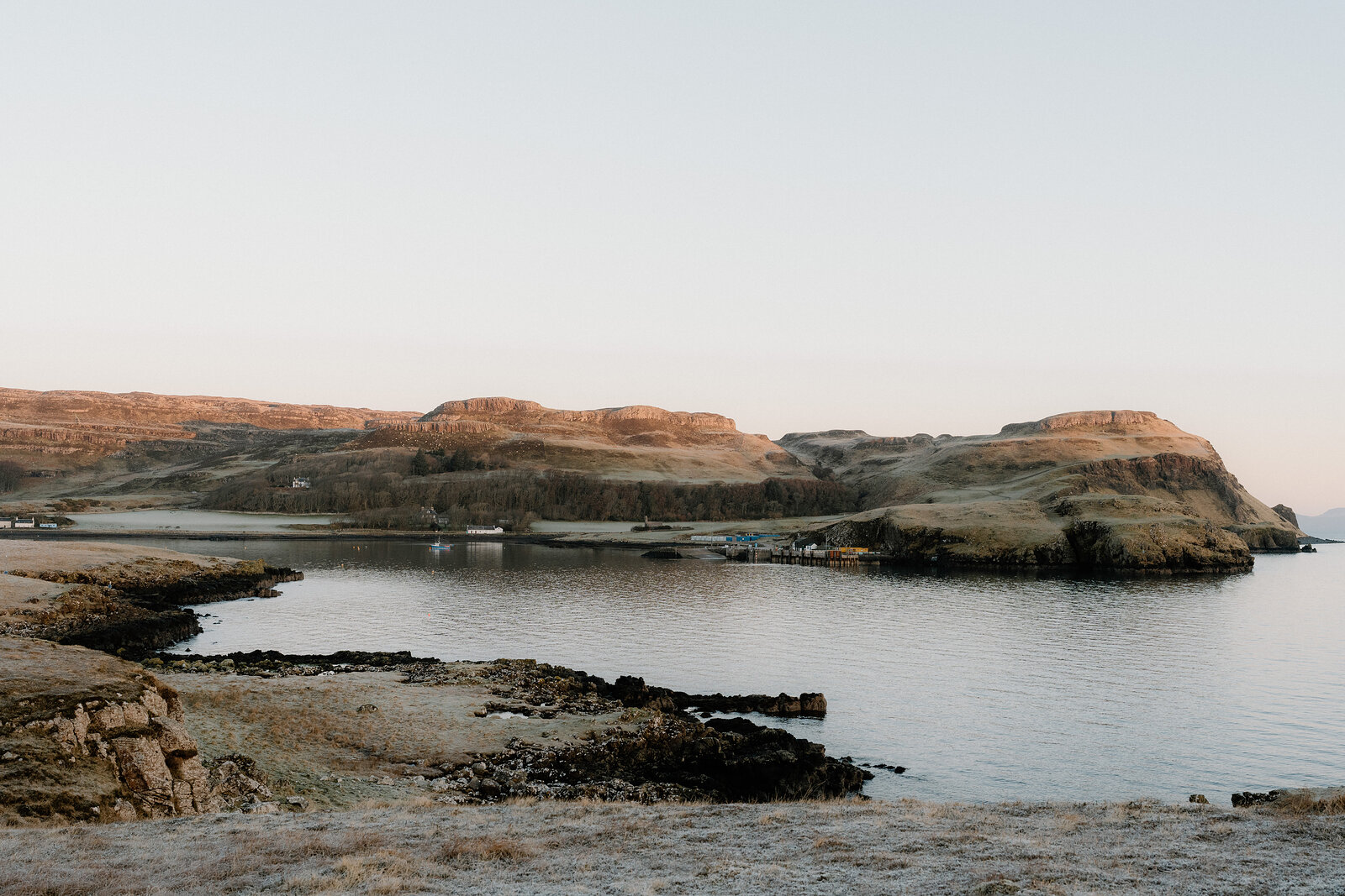 Boats in the sheltered bay below Sanday's low rocky headlands, in early light.