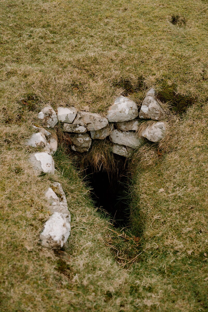 A souterrain opening in the turf, edged and roofed with pale stones.