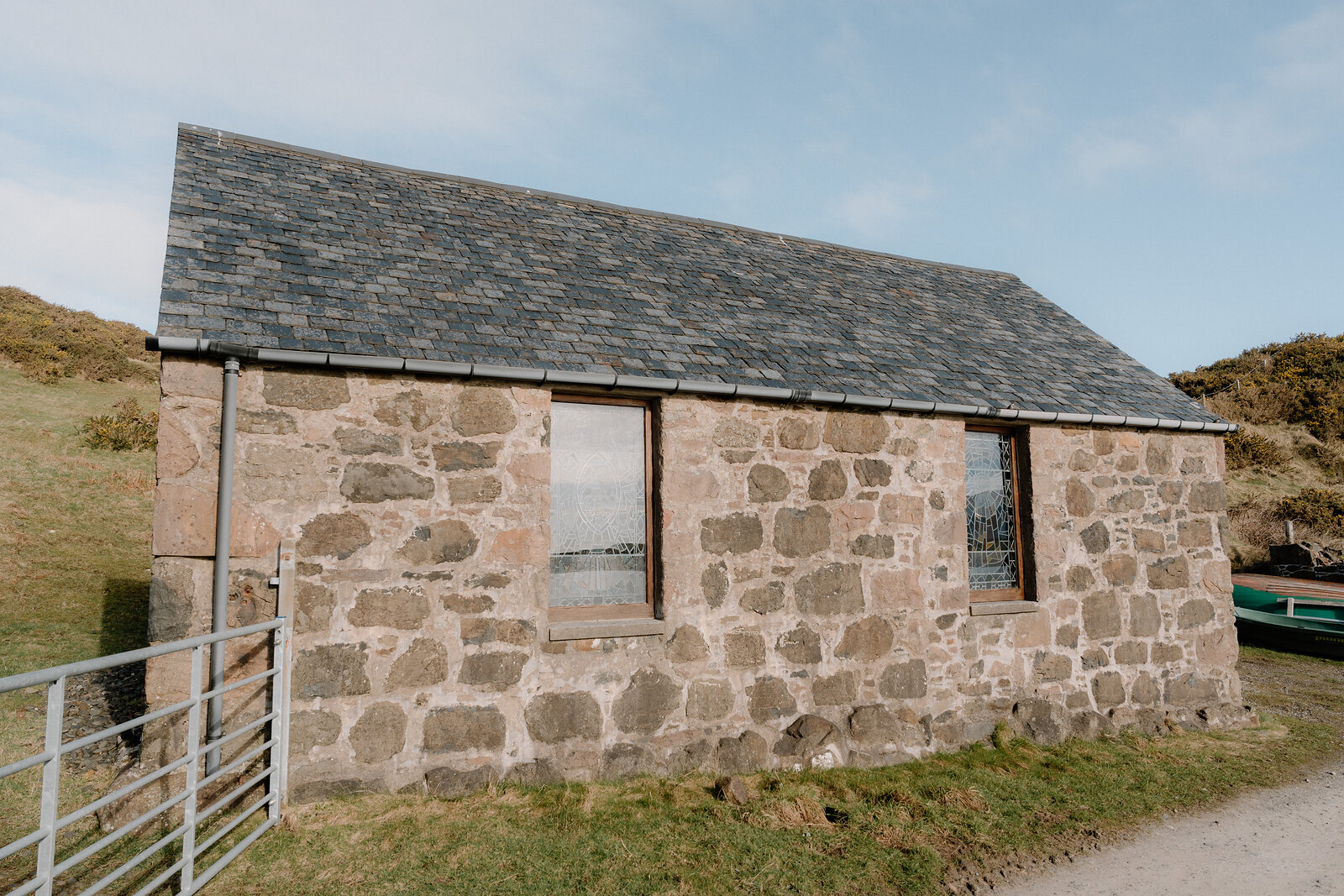 A stone bothy with slate roof and sash windows stands beside a metal gate on the Isle of Canna.