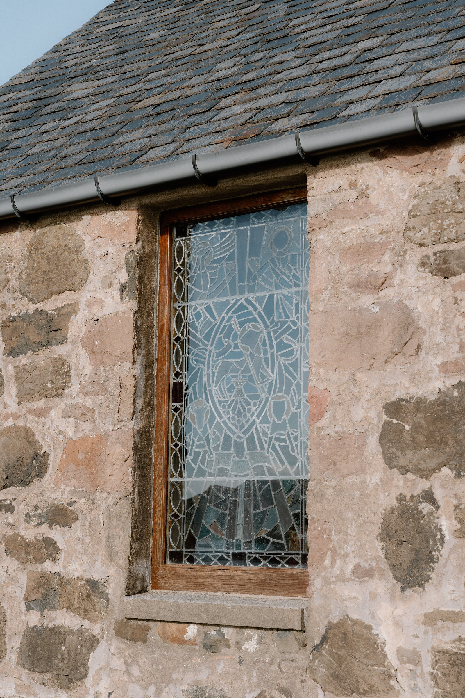 A leaded stained-glass window is set into the stone wall of a chapel on the Isle of Canna.