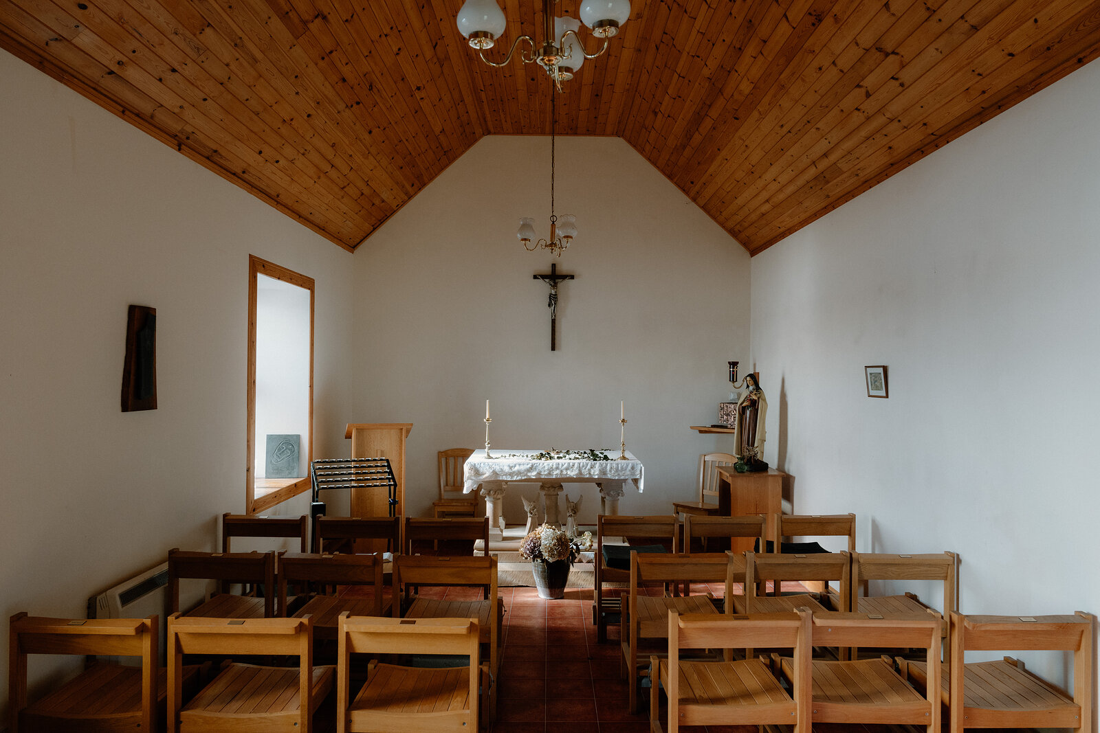 Wooden pews face a crucifix and altar beneath a timber-lined ceiling in a chapel on the Isle of Canna.