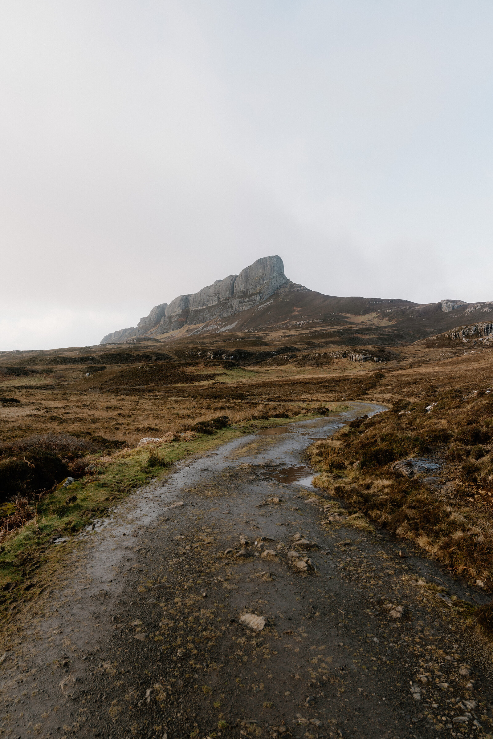 A gravel track winding through moorland towards a jagged rocky peak