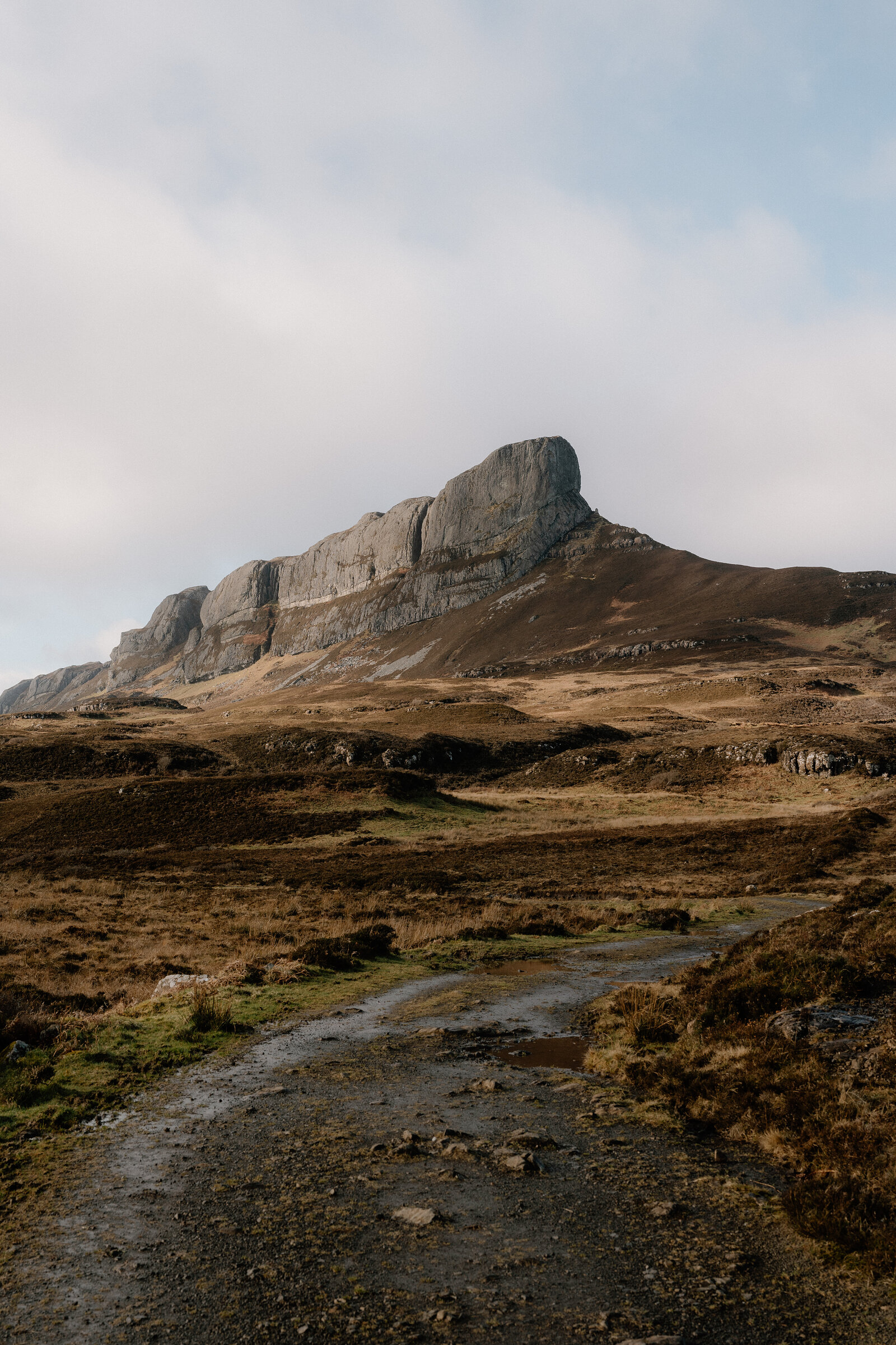 A jagged rocky peak rising above moorland, a gravel path winding towards it
