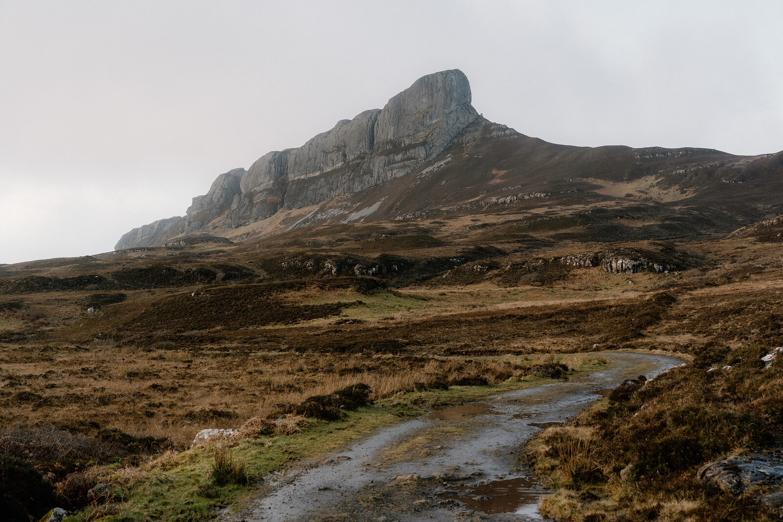 A jagged rocky peak rising above moorland, seen from a path across the hillside