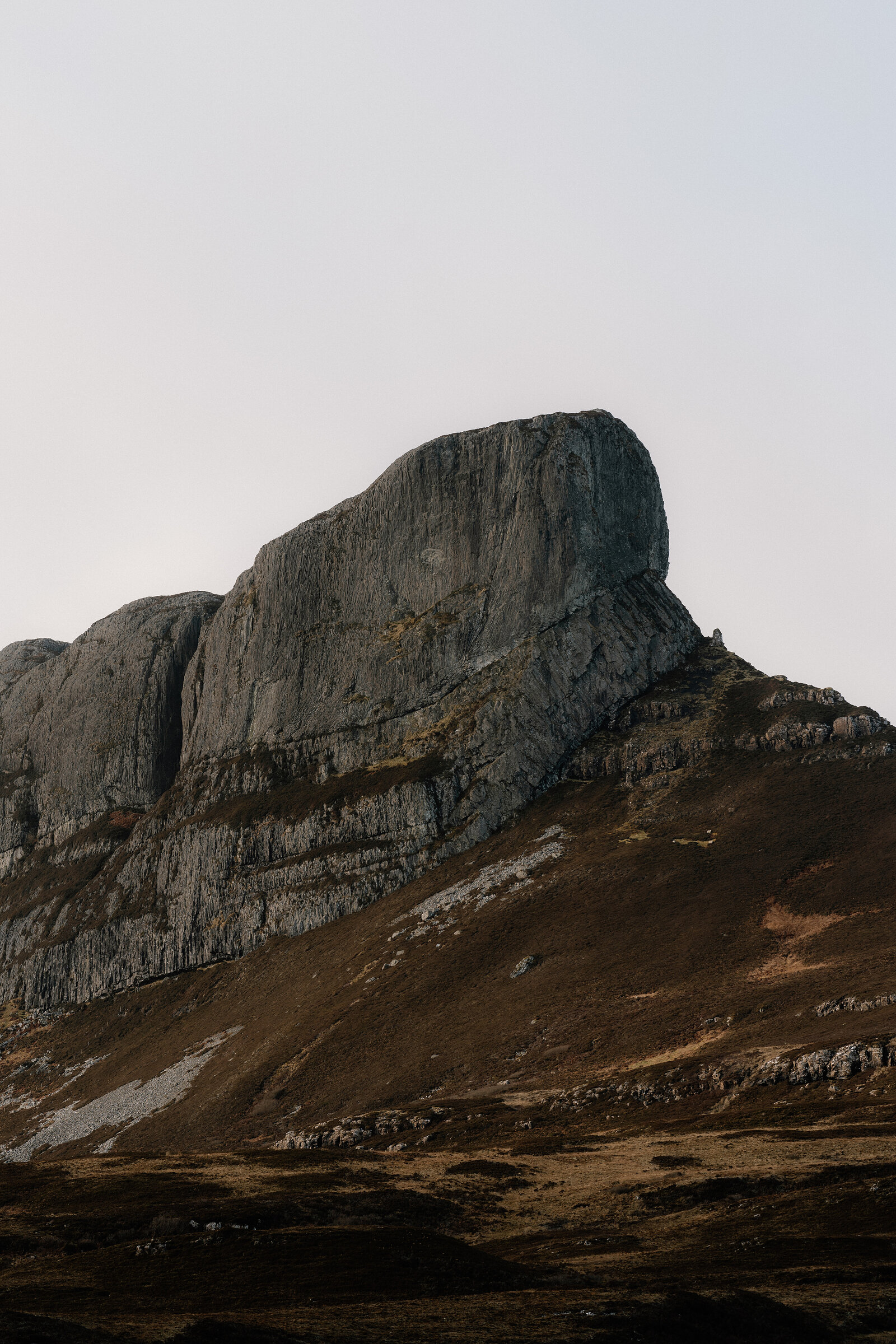 A jagged rocky peak rising above a heather-covered hillside.