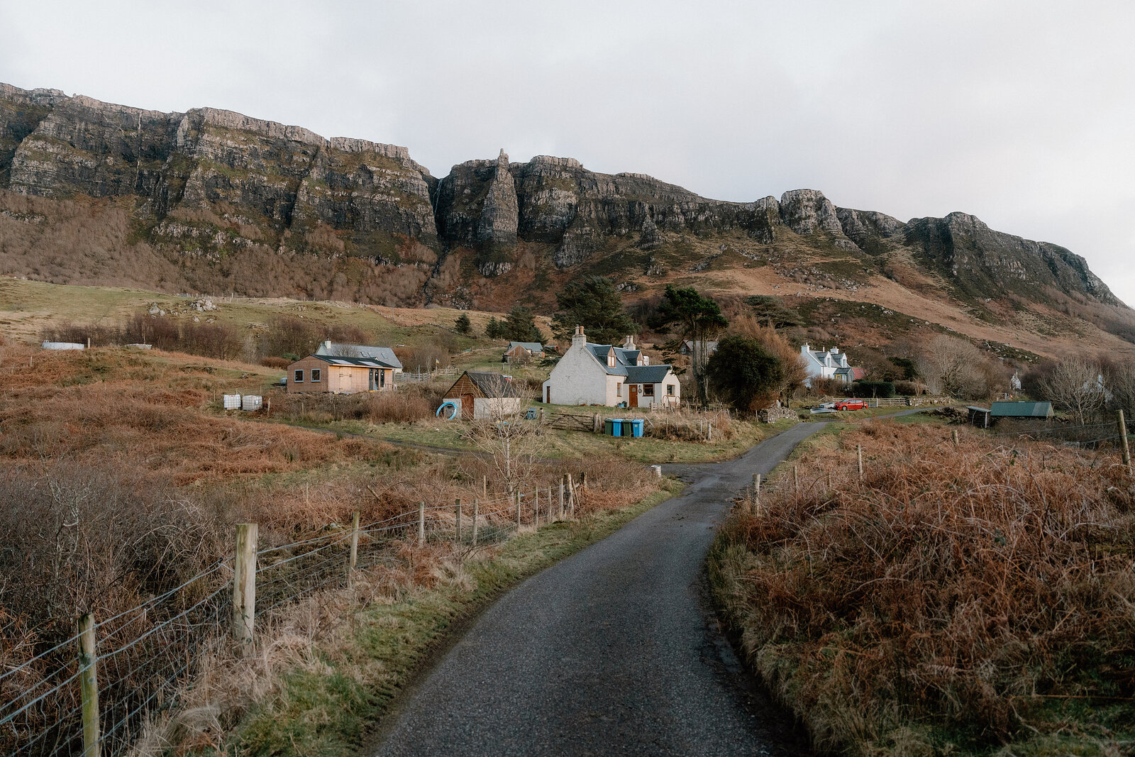 A row of white cottages set below layered rocky cliffs, a lane winding through the fields