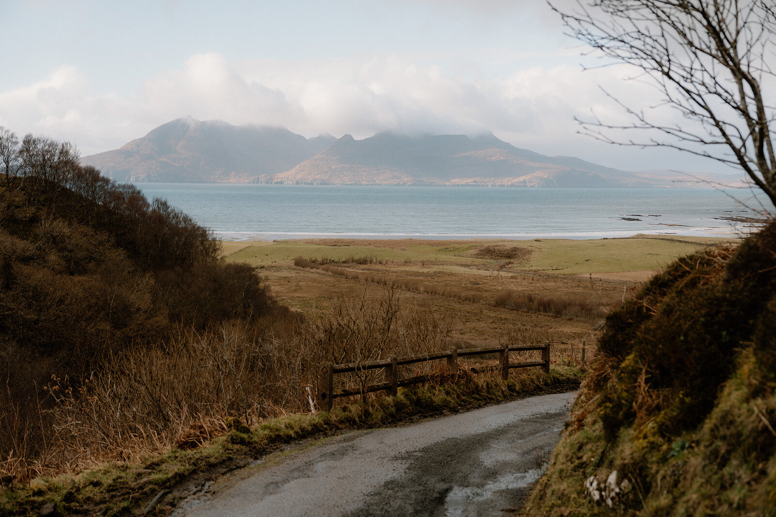 A wooden footbridge crossing a track above a bay, hills rising across the water