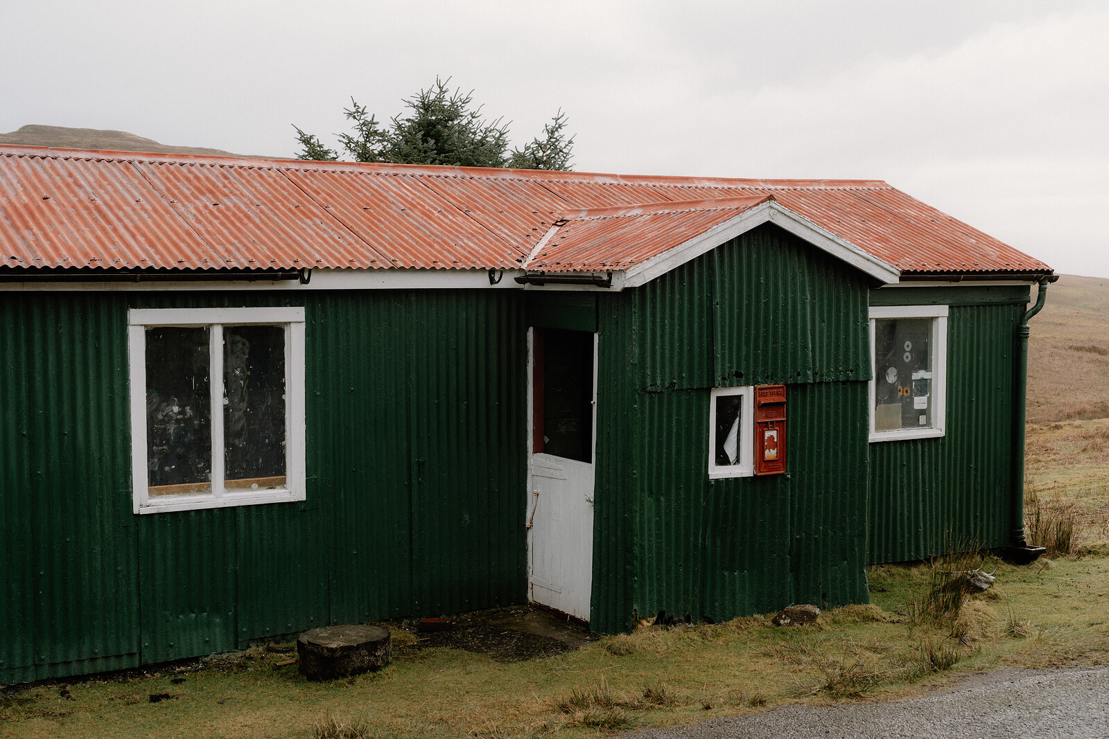 A green corrugated cottage with a red postbox set into the wall beside the door