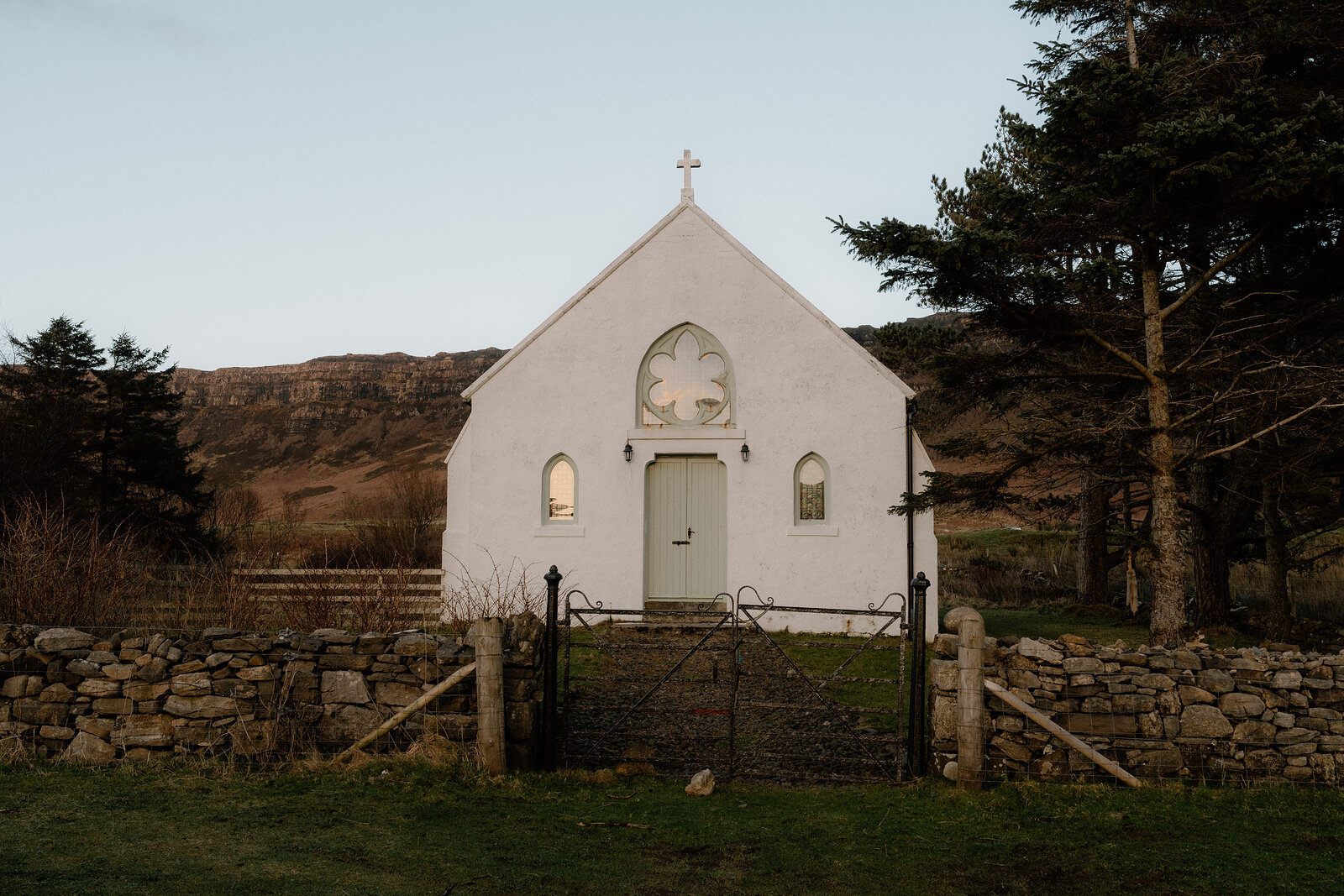 A small whitewashed church with a cross-shaped window stands behind a dry-stone wall.