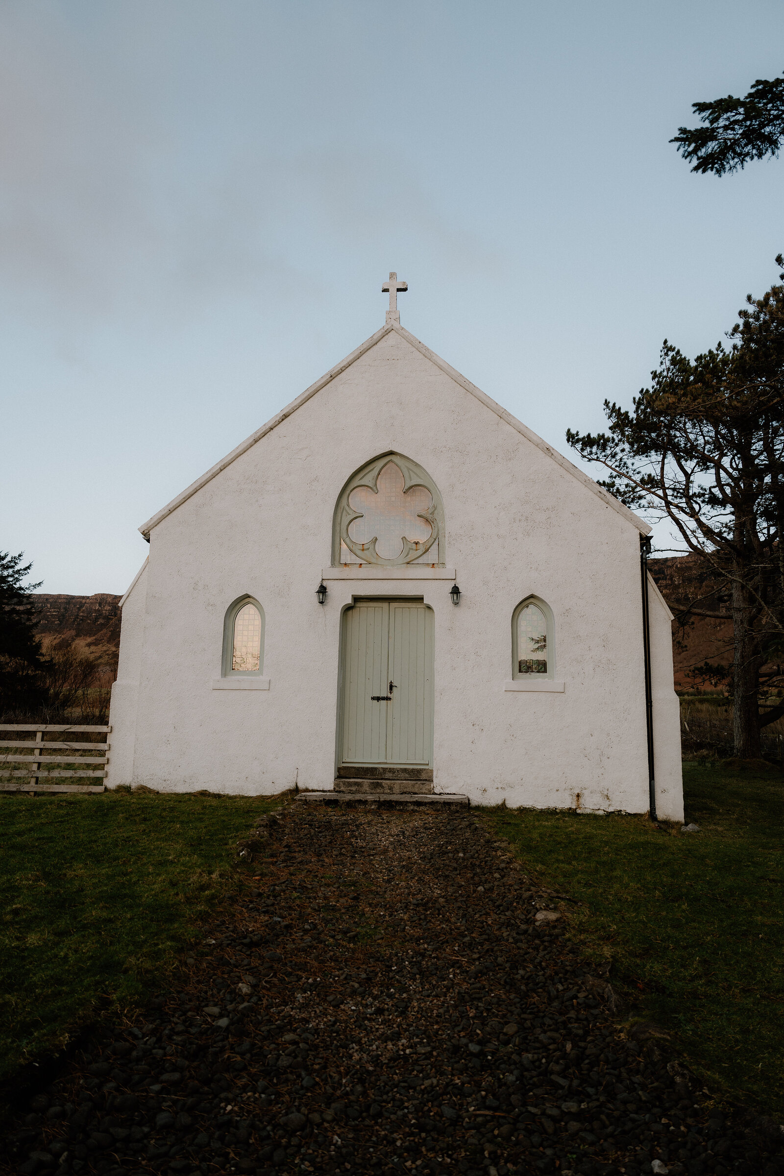 A small whitewashed church's cross and quatrefoil window rise against the sky.