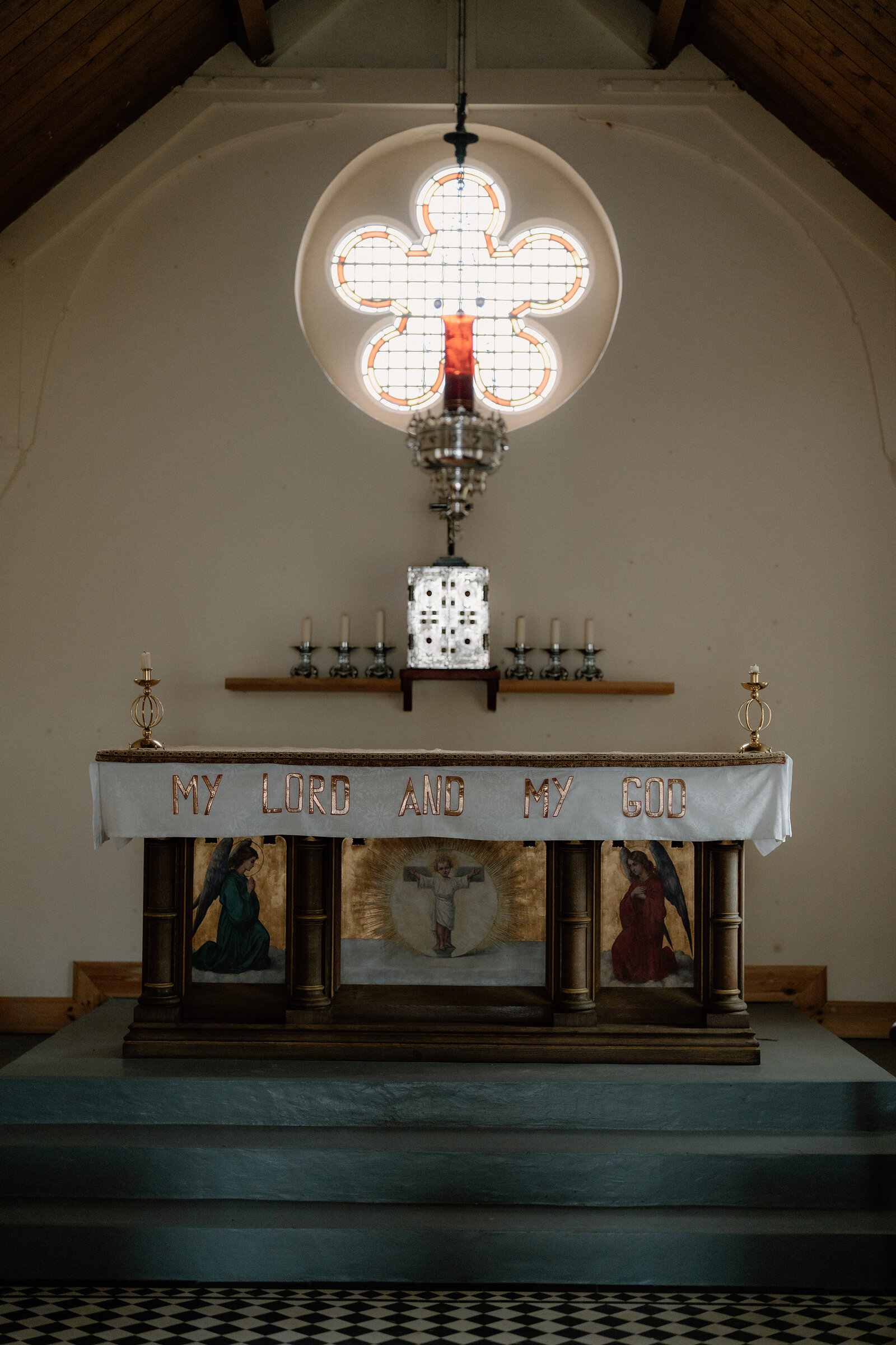 An altar cloth reading 'My Lord and My God' sits beneath a glowing quatrefoil rose window.