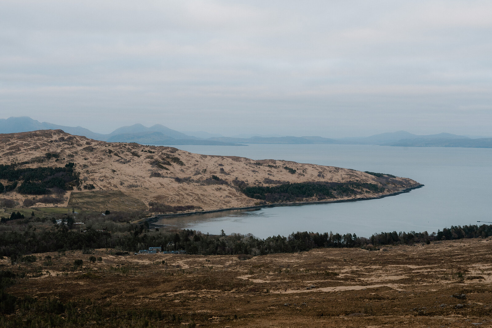A grassy headland curves into the sea beneath distant mountains on the Isle of Rum.