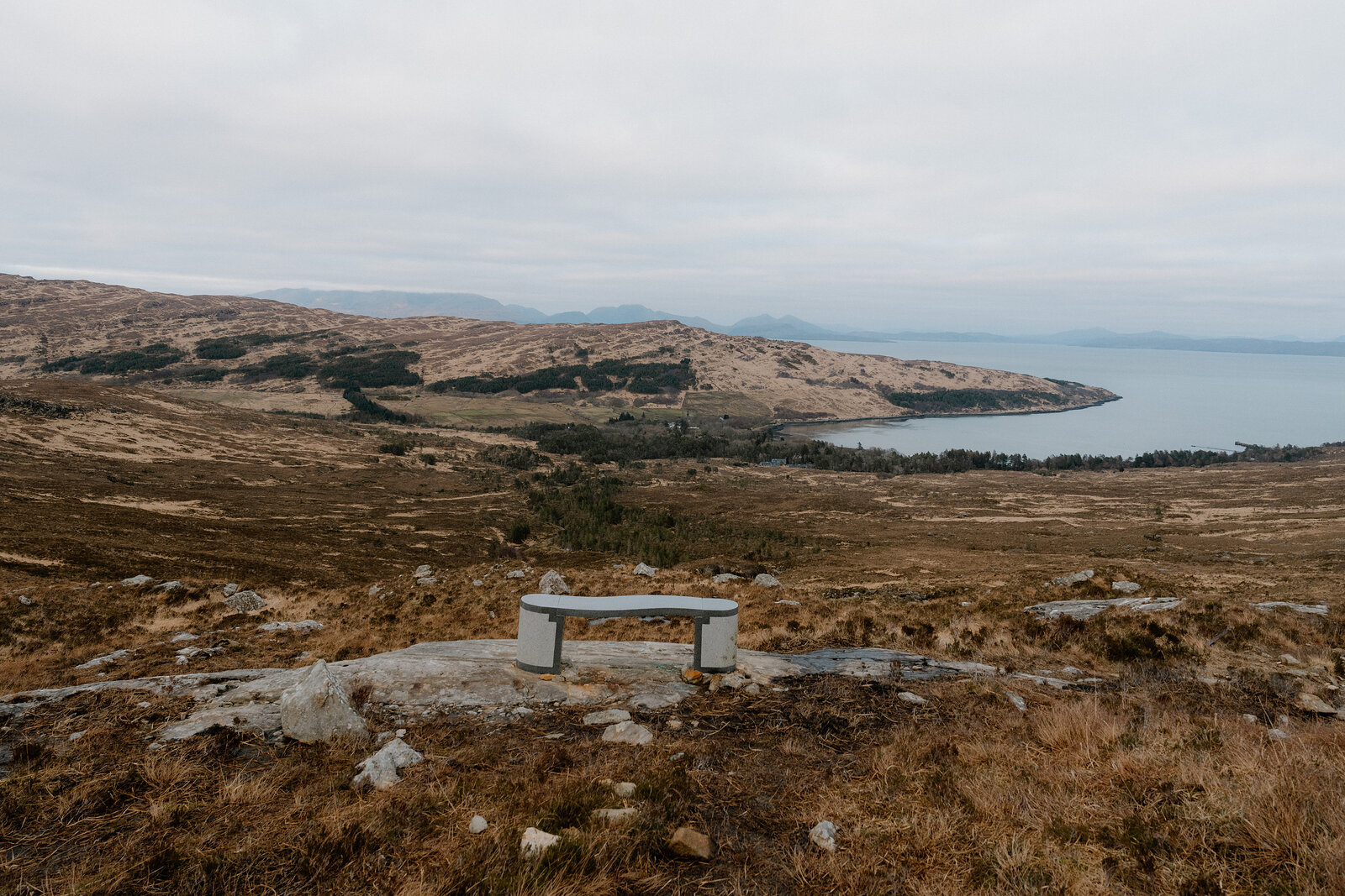 A stone bench overlooks a curving bay and distant hills on the Isle of Rum.