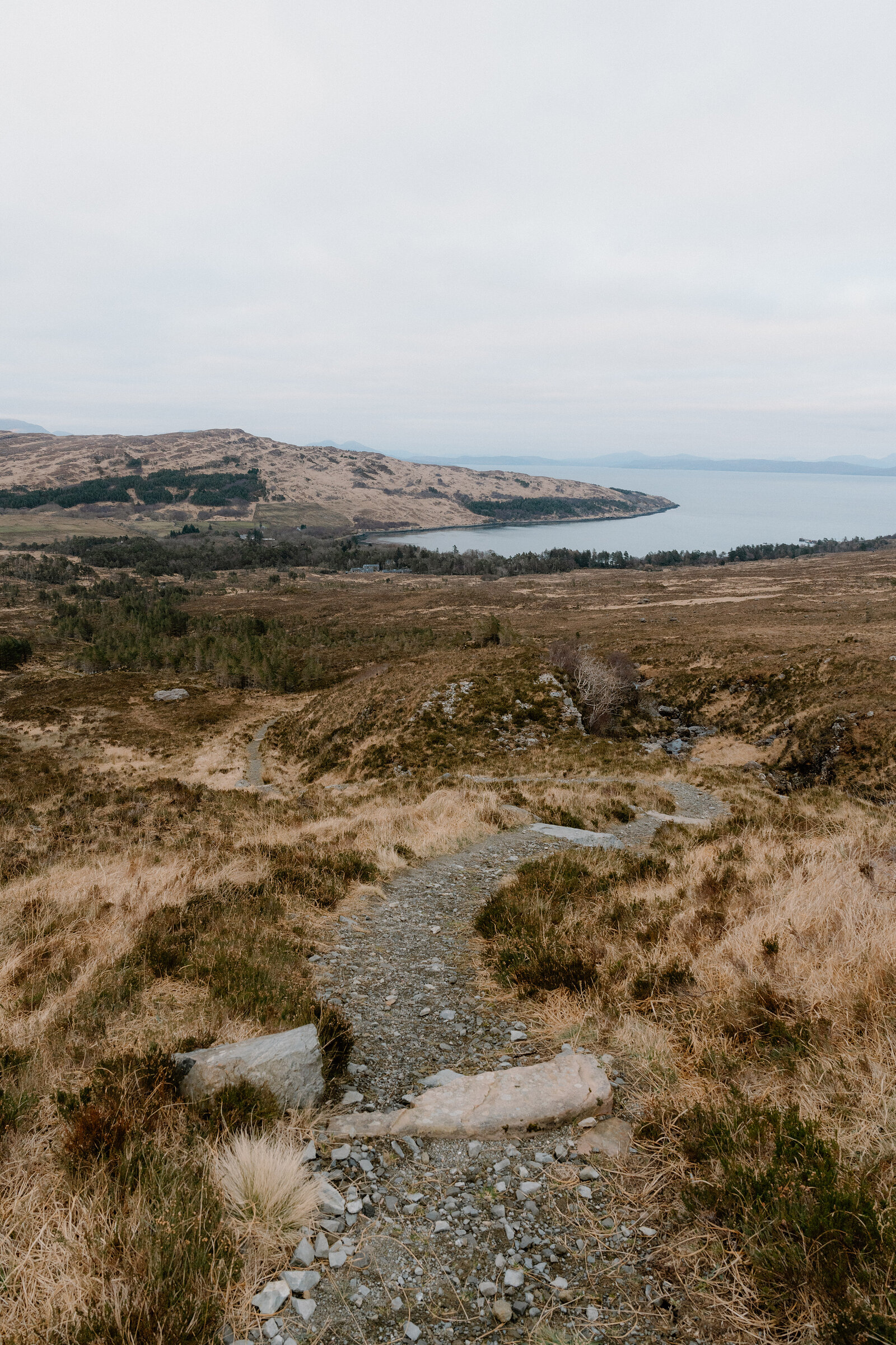 A gravel path winds across moorland above a wooded bay on the Isle of Rum.