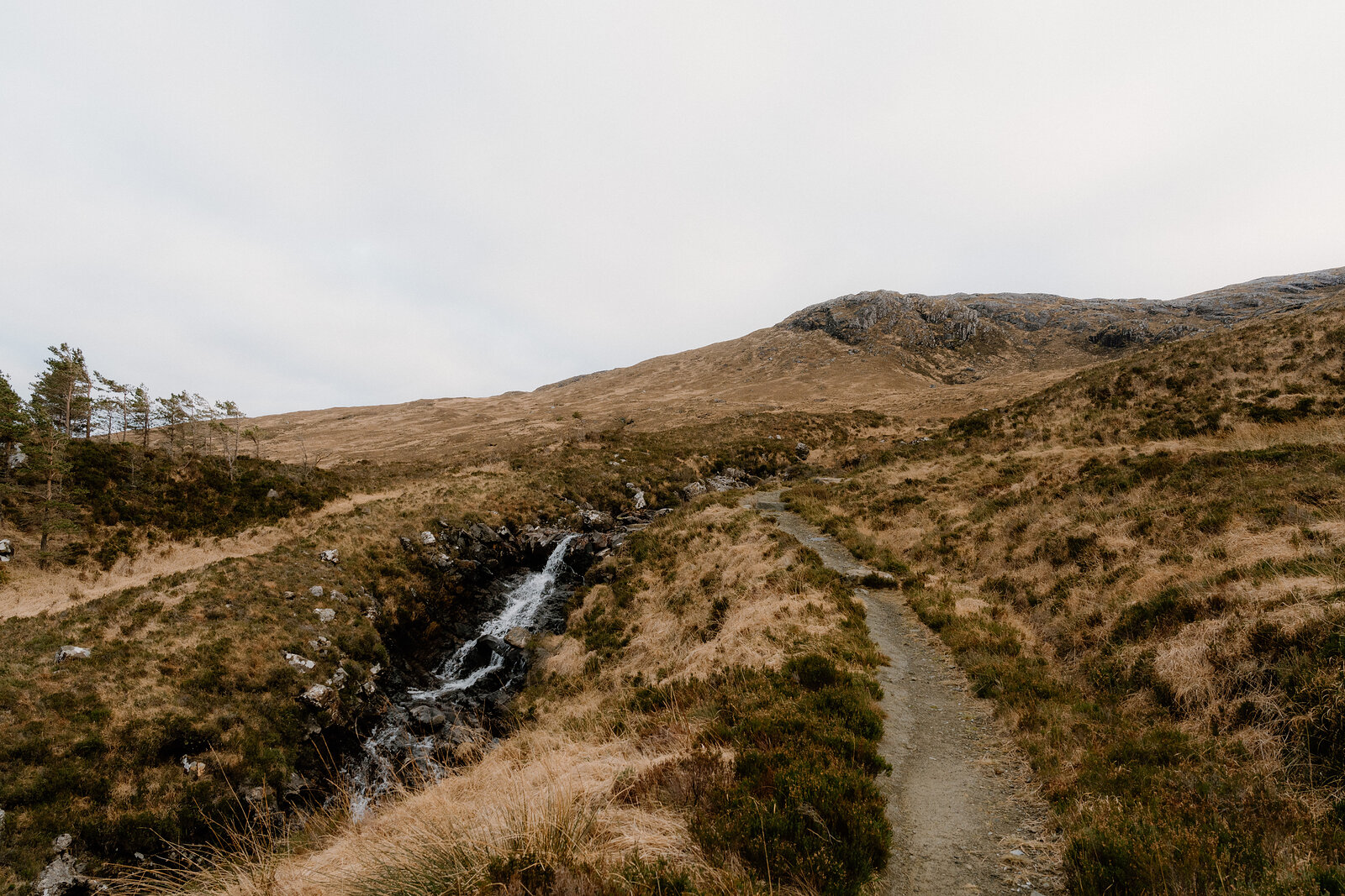 A path follows a small waterfall through open moorland on the Isle of Rum.