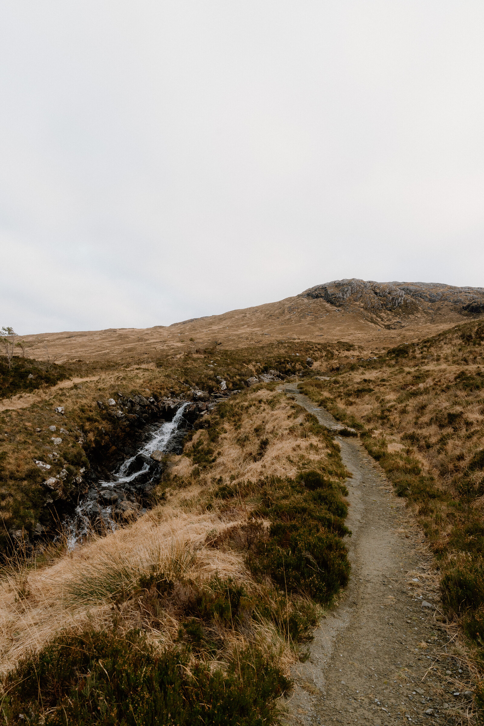 A gravel path winds past a burn toward a rocky hilltop on the Isle of Rum.
