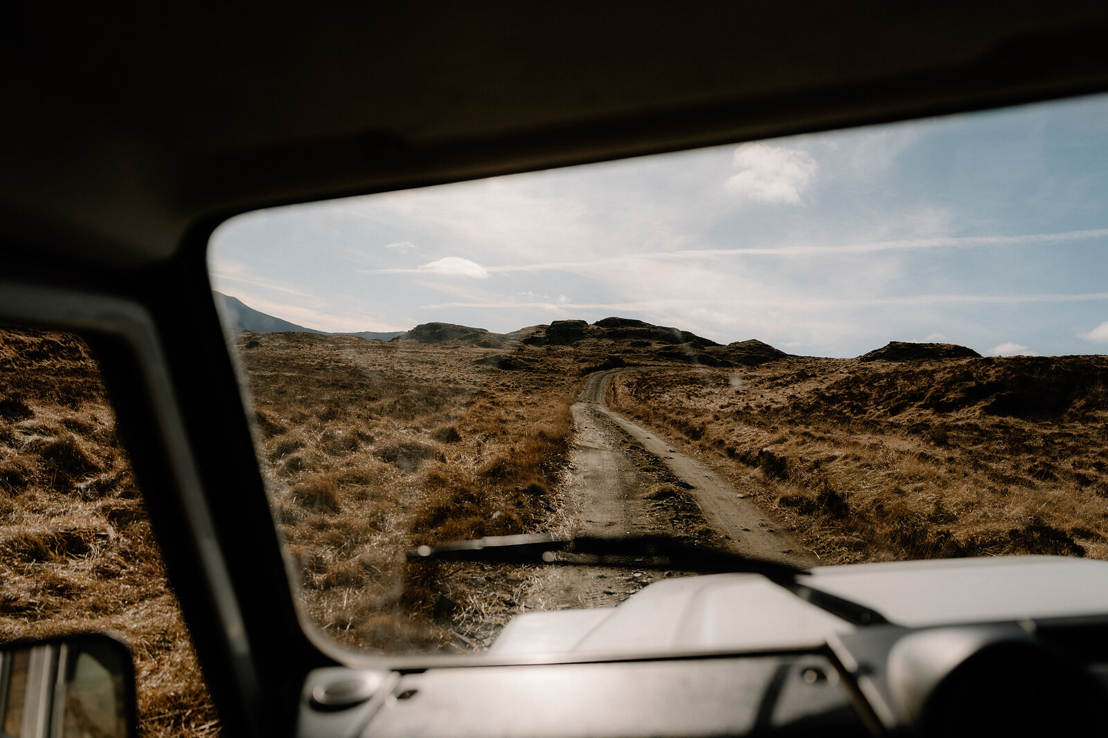 A dirt track winds across open moorland, seen through a vehicle's windscreen on the Isle of Rum.