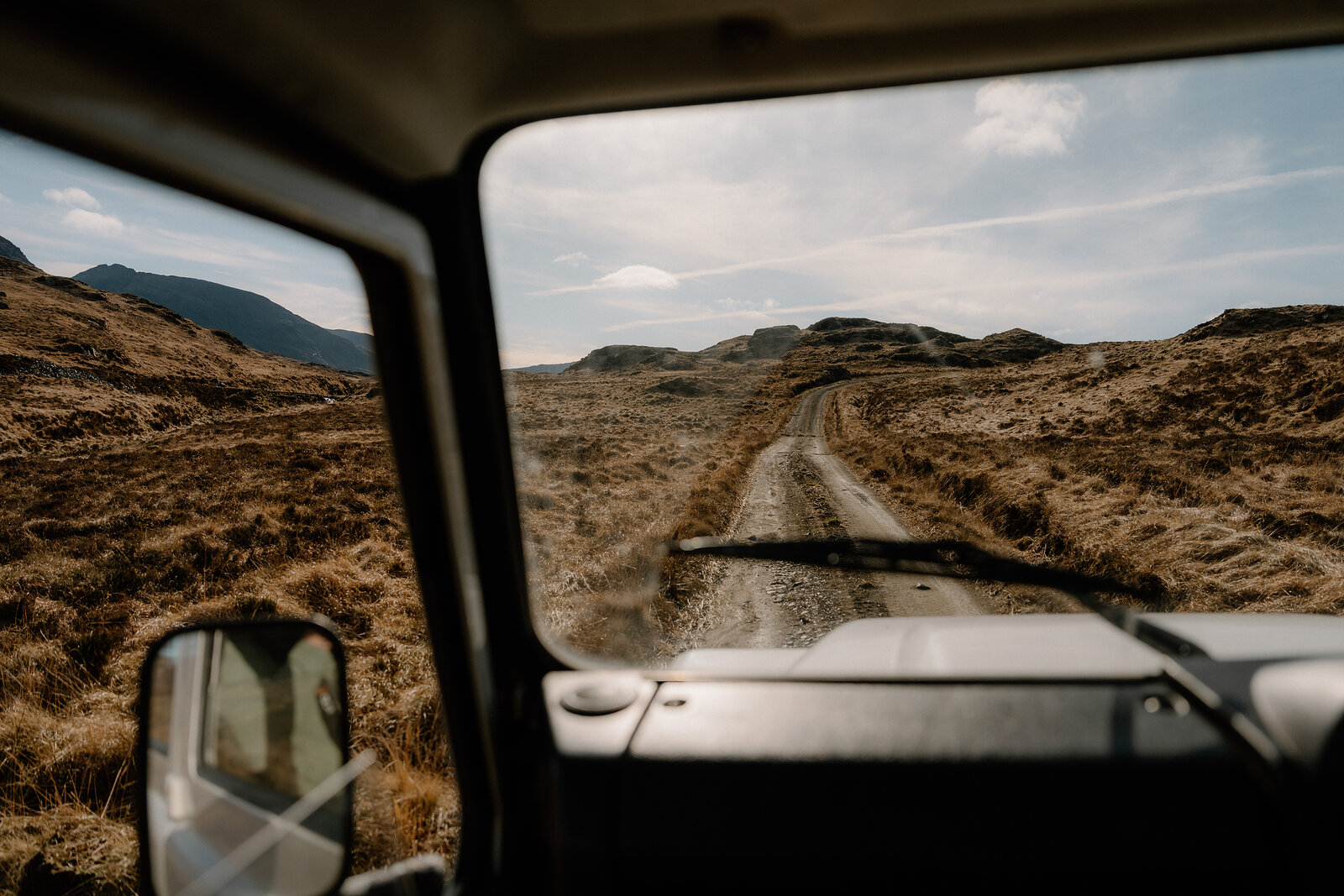 A dirt track winds through hills, seen from inside a vehicle on the Isle of Rum.