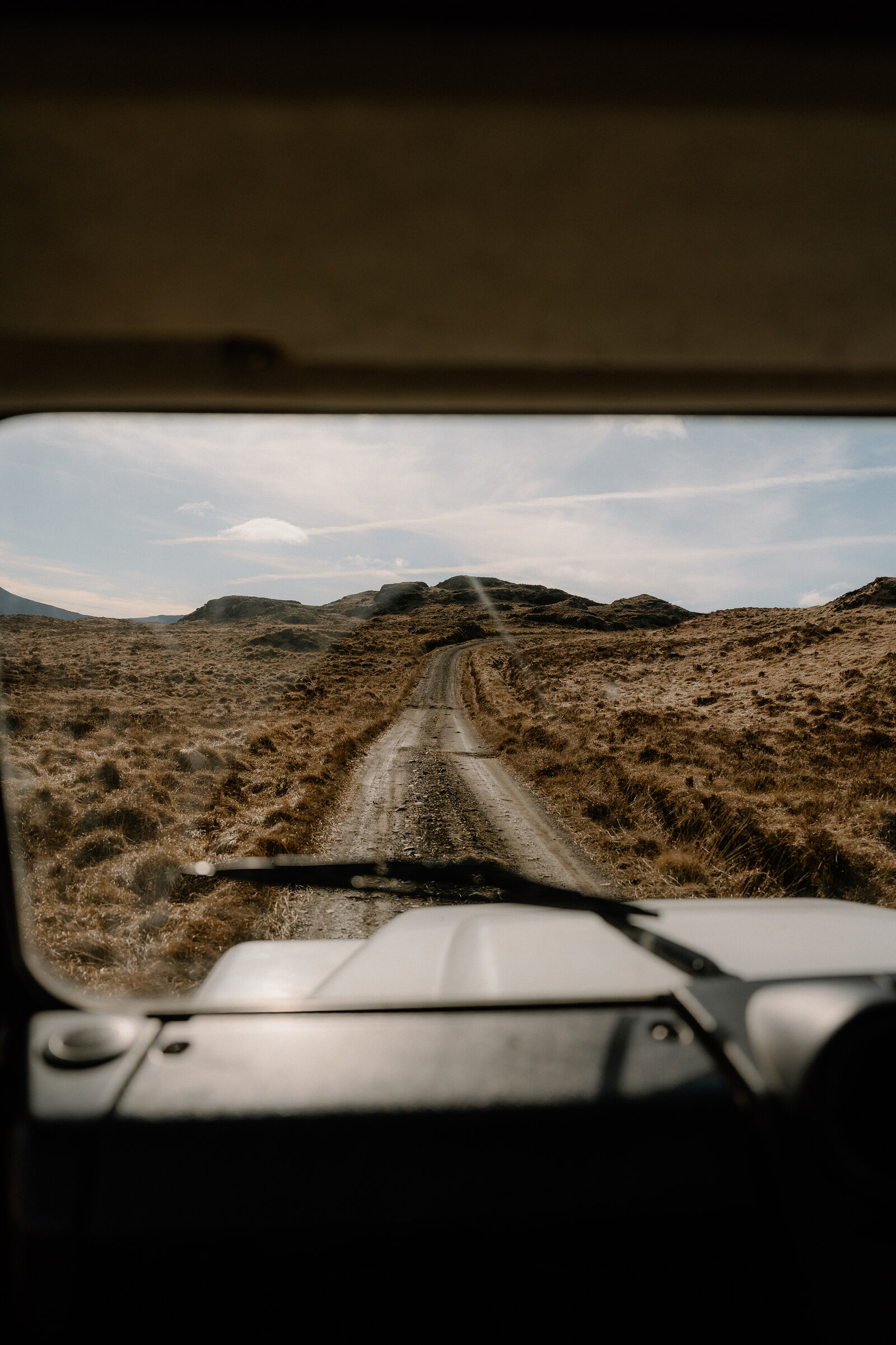 A dirt track curves through open moorland toward hills, seen from inside a vehicle on the Isle of Rum.