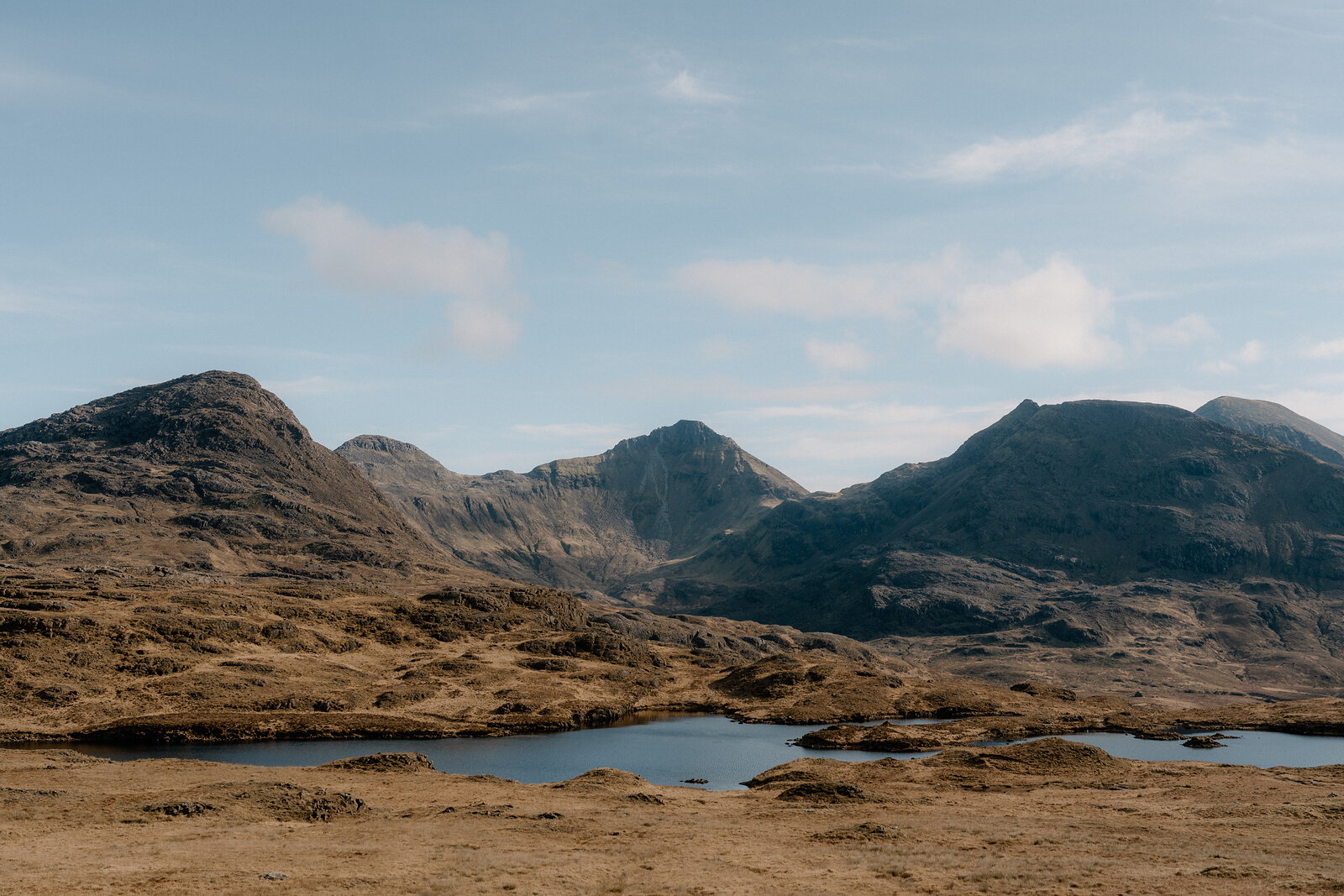 A small loch reflects the sky amid golden moorland on the Isle of Rum, mountains rising behind.