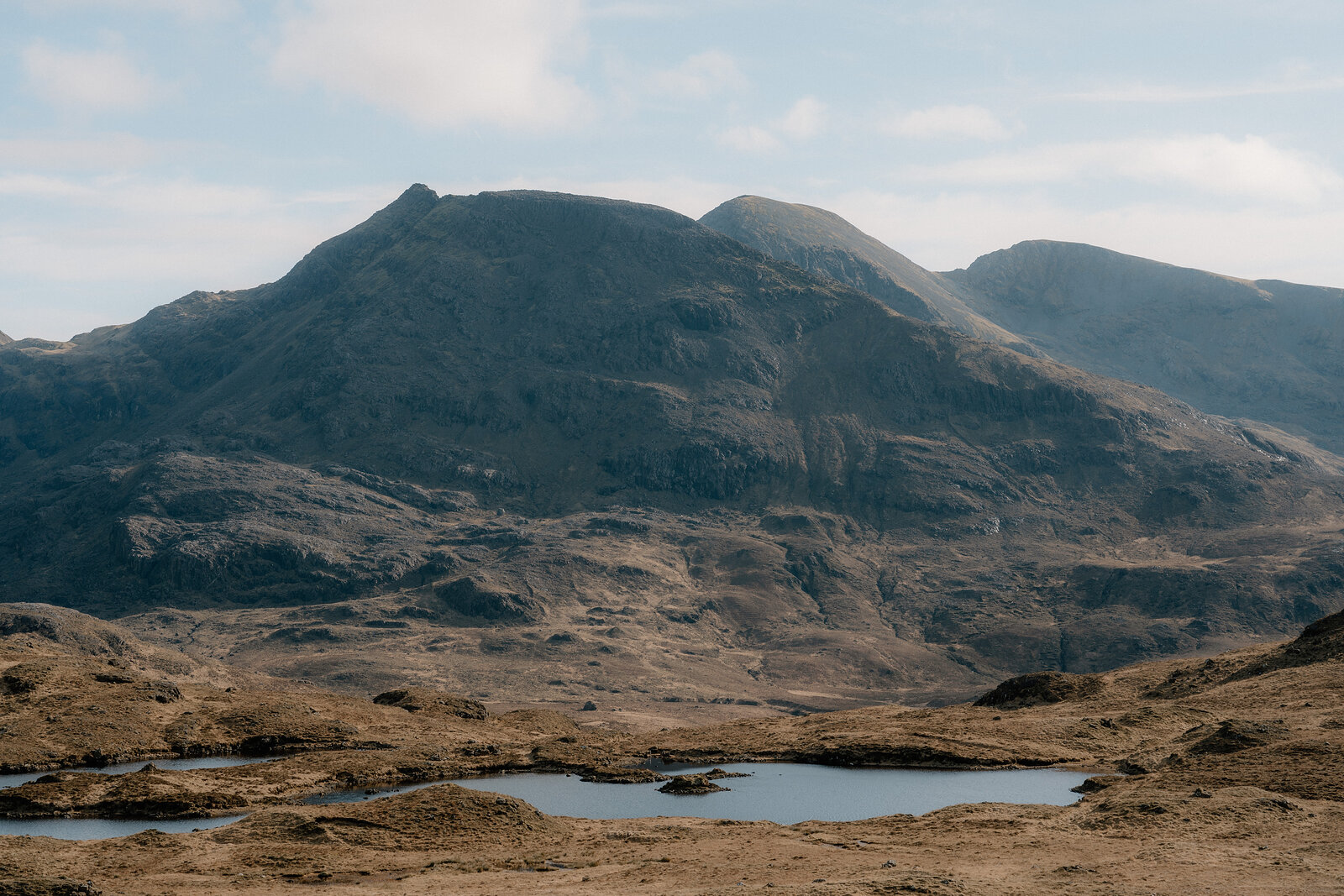 Jagged mountain peaks rise above a small loch amid golden moorland on the Isle of Rum.