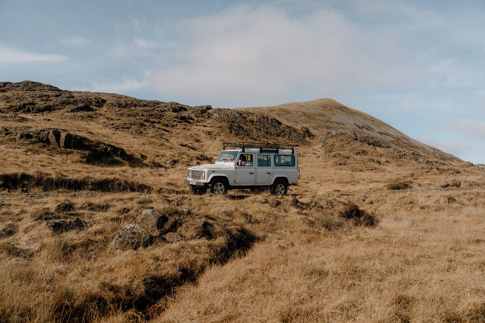 A white Land Rover is parked on a hillside track on the Isle of Rum, a mountain rising behind.