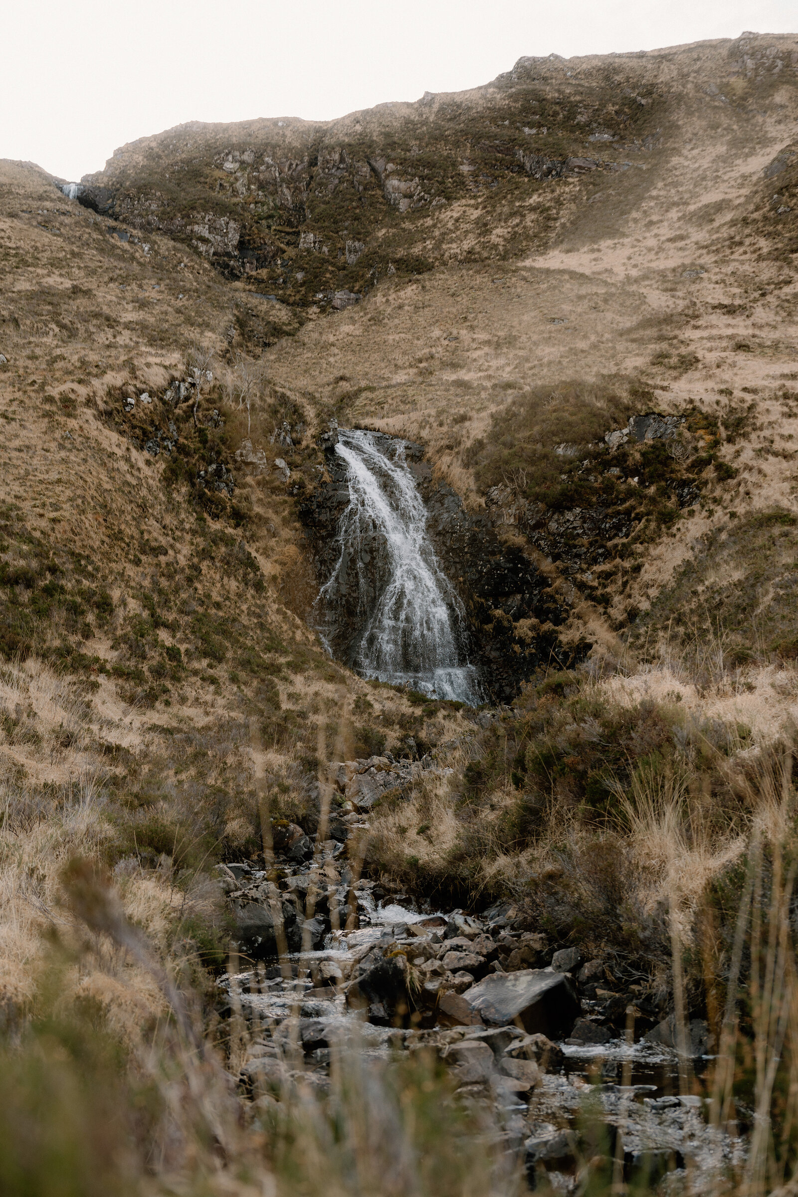 A waterfall cascades over dark rock down a grassy hillside on the Isle of Rum.