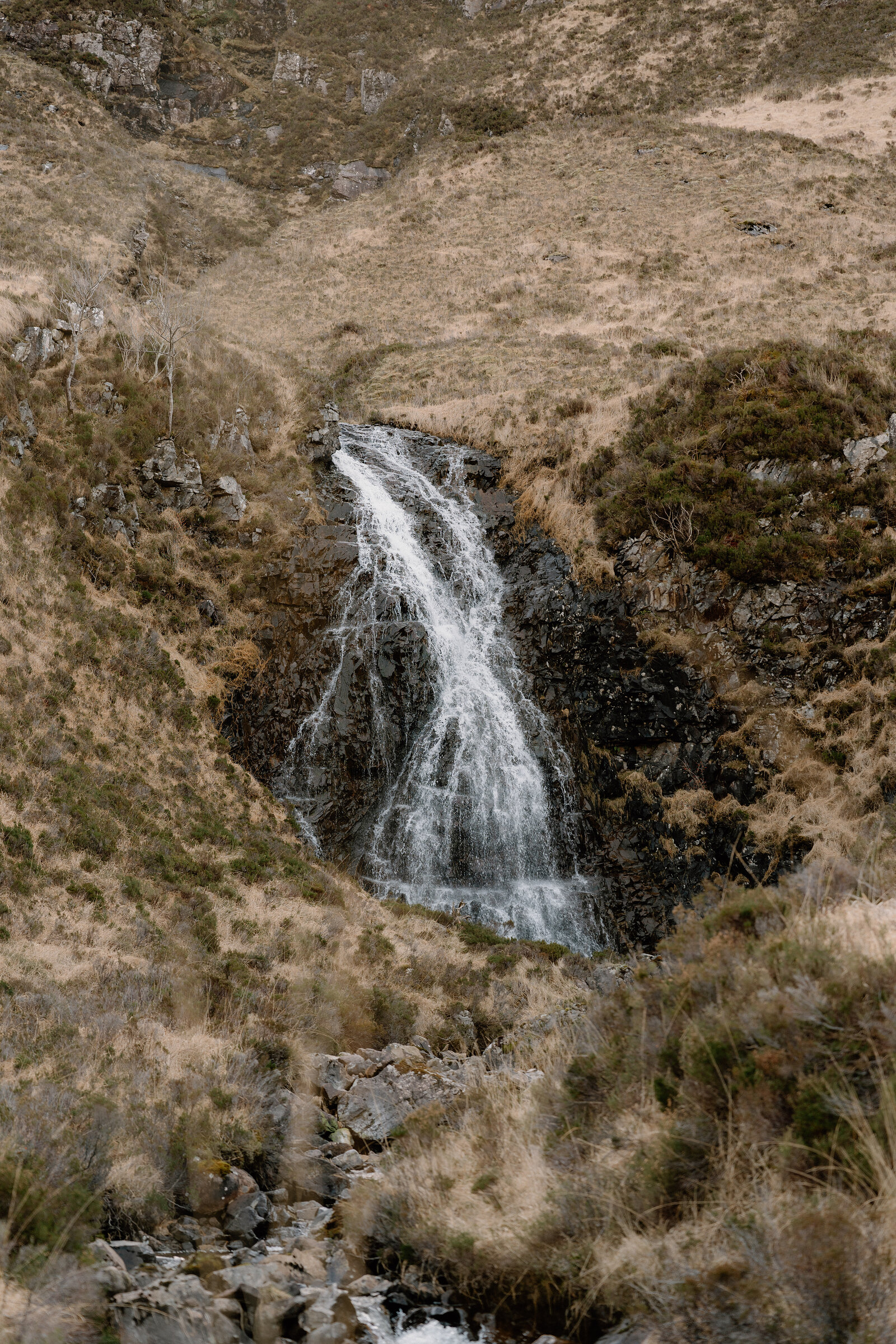 A waterfall tumbles down a rocky gully between grassy slopes on the Isle of Rum.