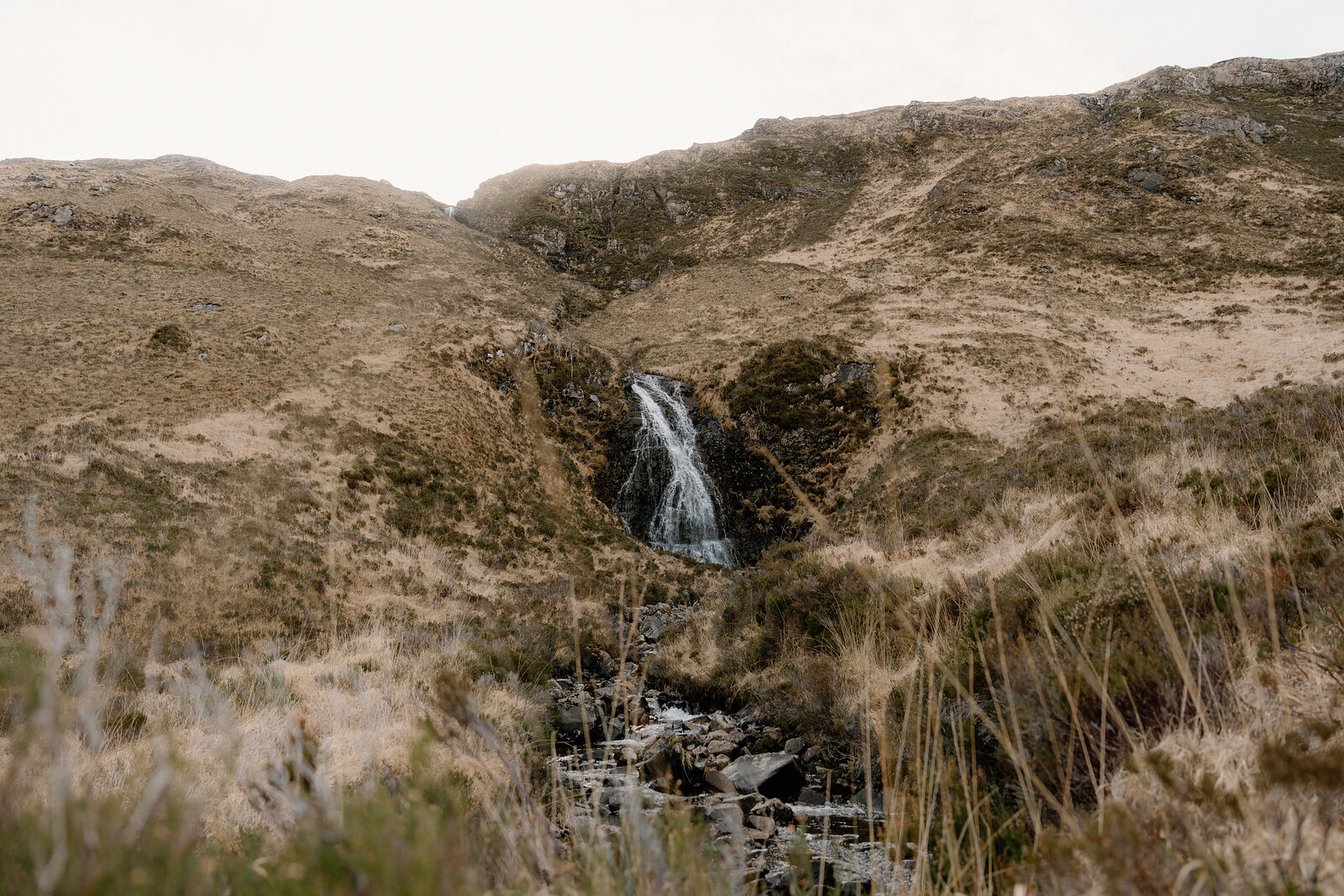 A waterfall streaks down a rocky gully on a grassy hillside on the Isle of Rum.