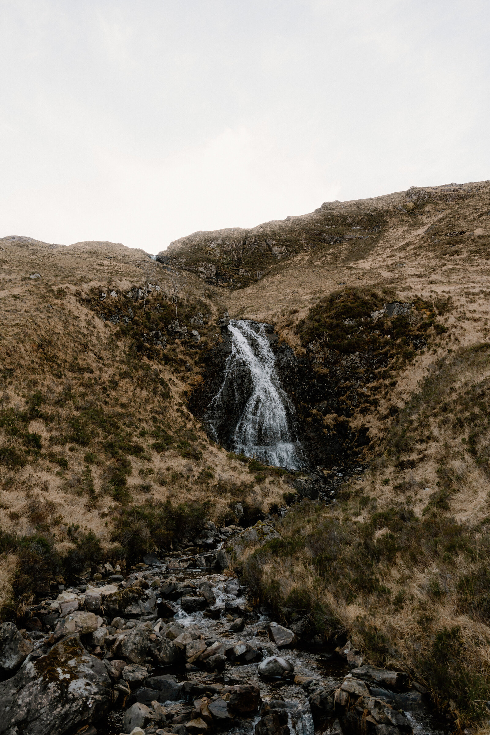 A waterfall streaks down a rocky gully on a grassy hillside on the Isle of Rum.