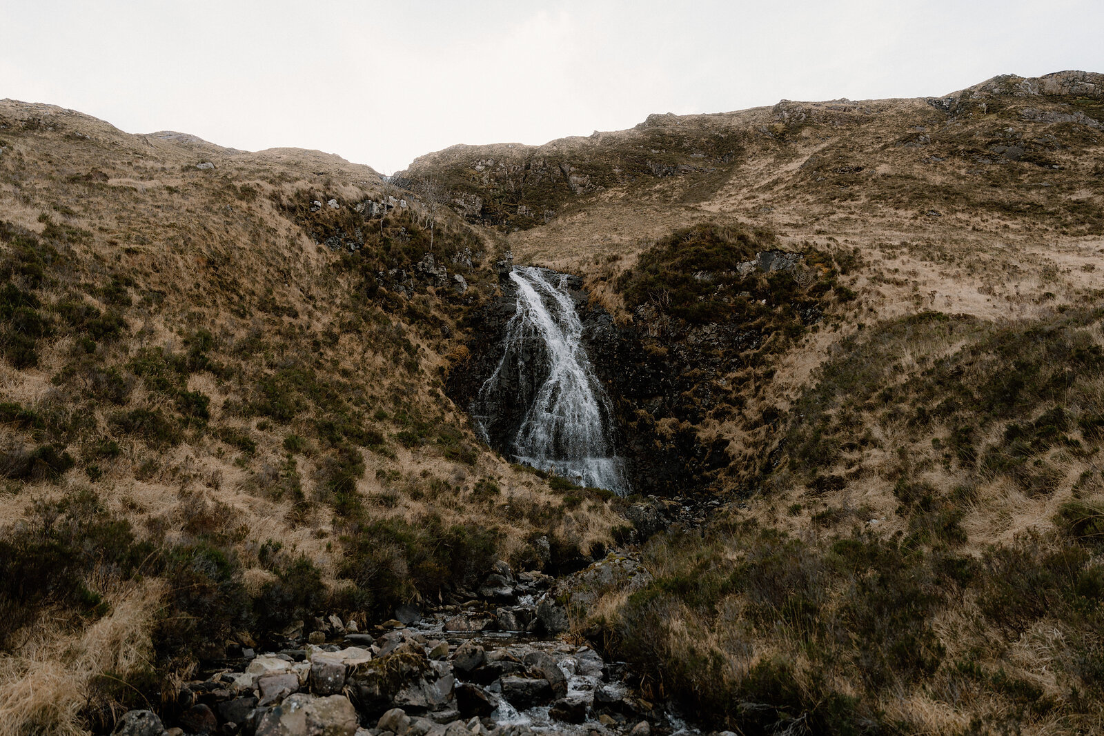 A waterfall tumbles down a mossy gully on a grassy hillside on the Isle of Rum.