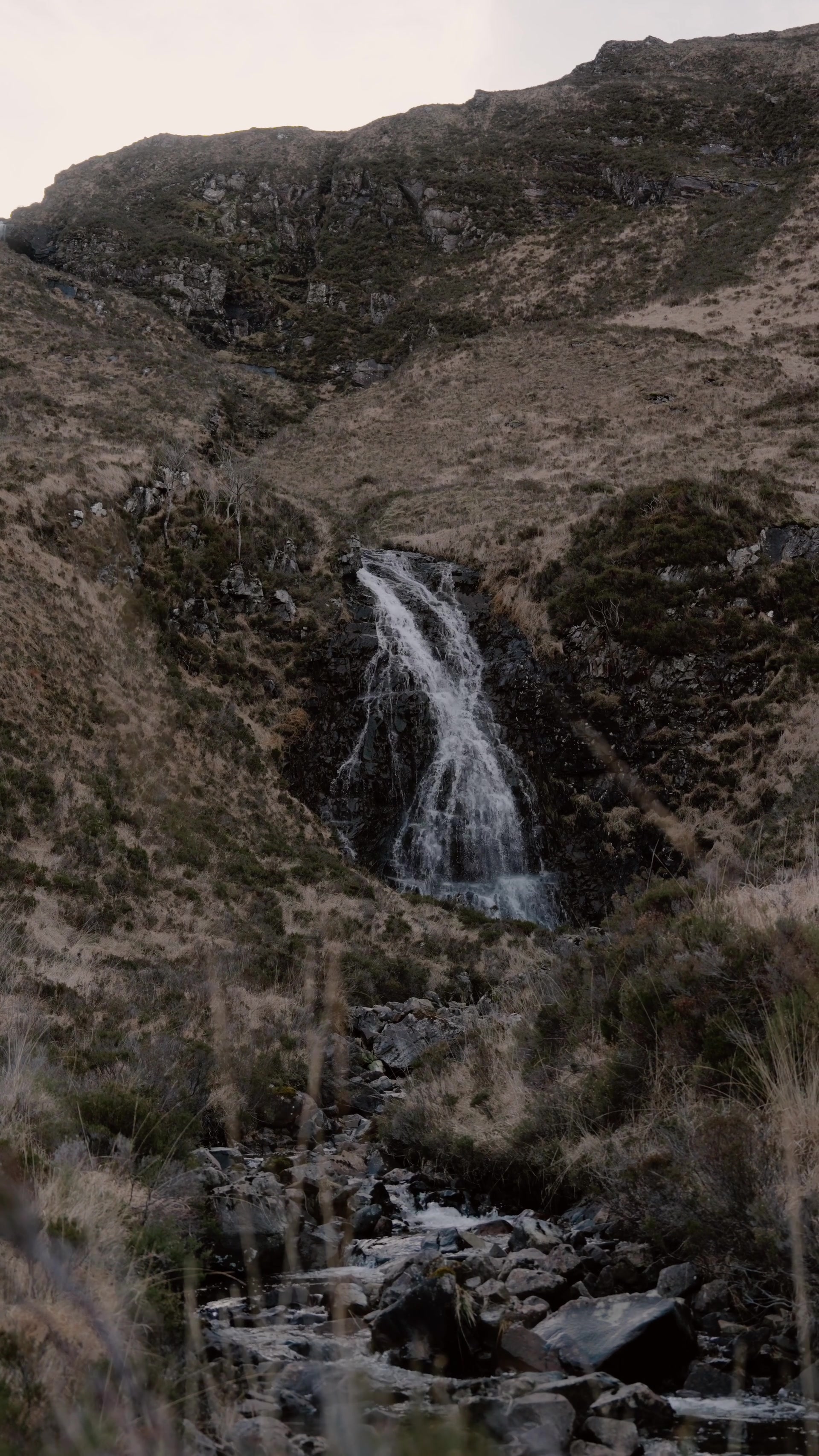 a waterfall dropping down a dark rock face on a dry moorland hillside on Rum