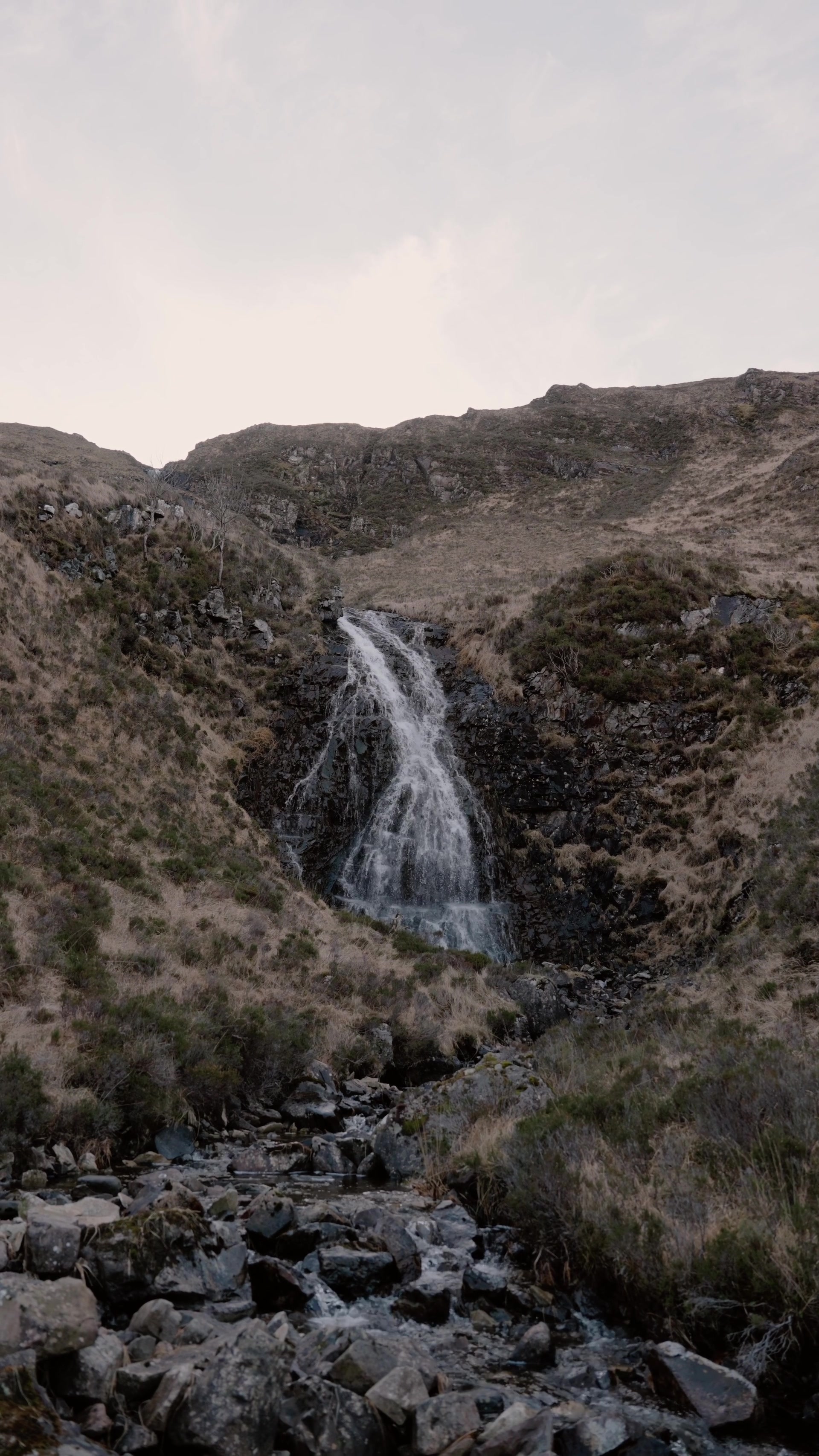 a wider view of the same waterfall spilling down the hillside gully into a rocky burn below