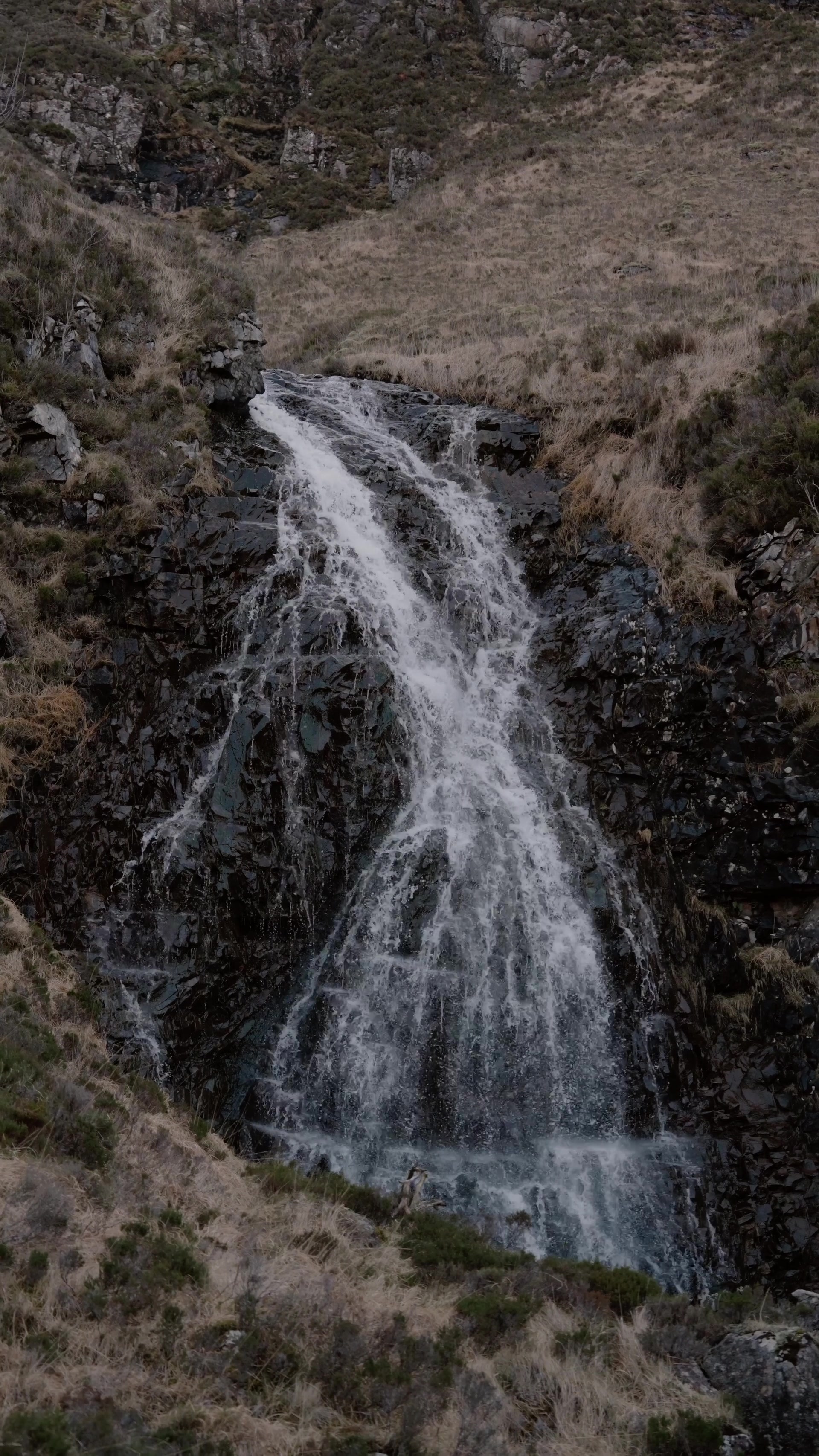 a waterfall spilling down a dark rocky gully between banks of dry moorland grass
