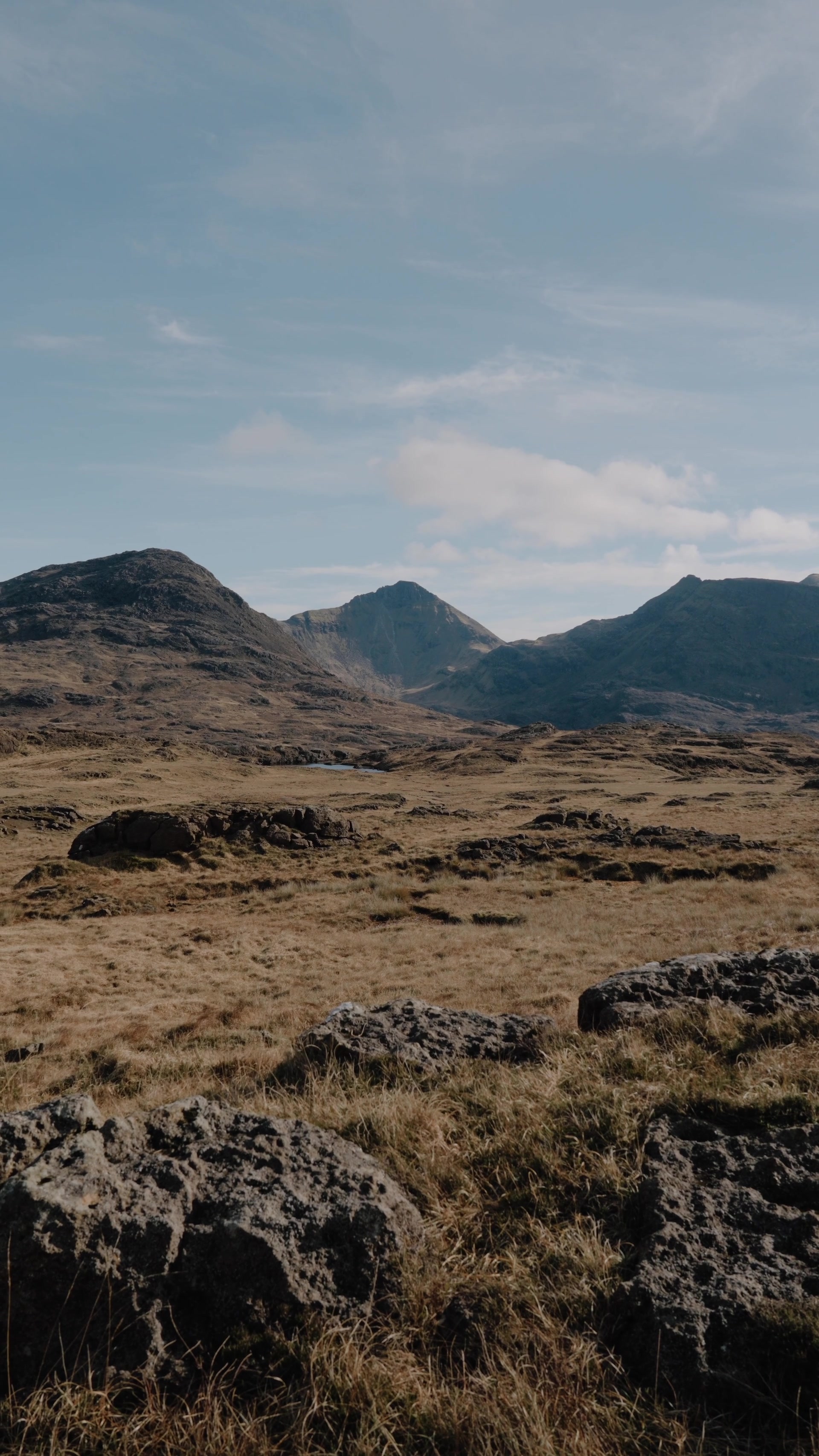 three rugged mountain summits rising above open moorland, a small loch nestled at their foot