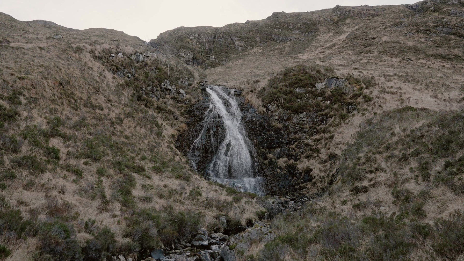 a narrow waterfall dropping through a rocky gully on a dry moorland hillside