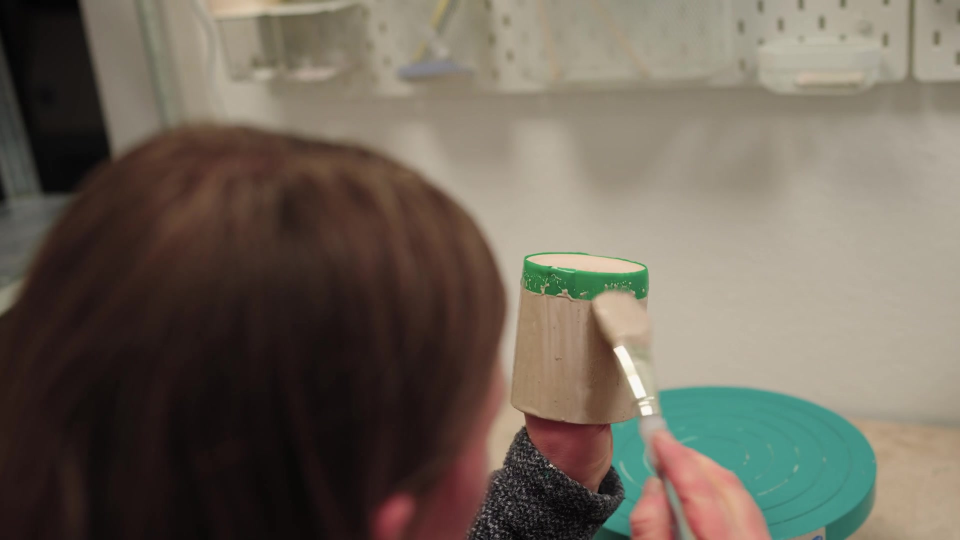 A potter brushing glaze onto a green-rimmed clay cup at a banding wheel