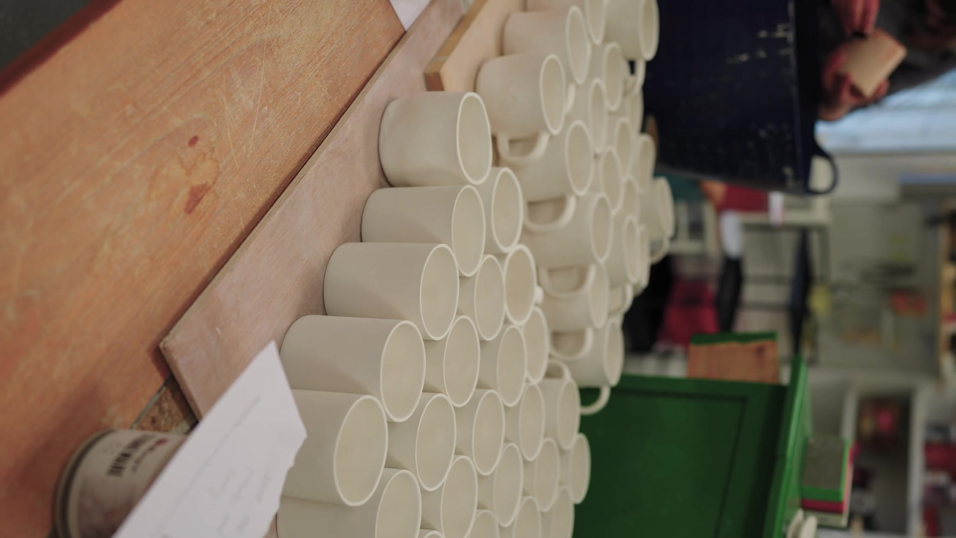 Rows of unglazed pottery mugs cool on a workshop shelf.