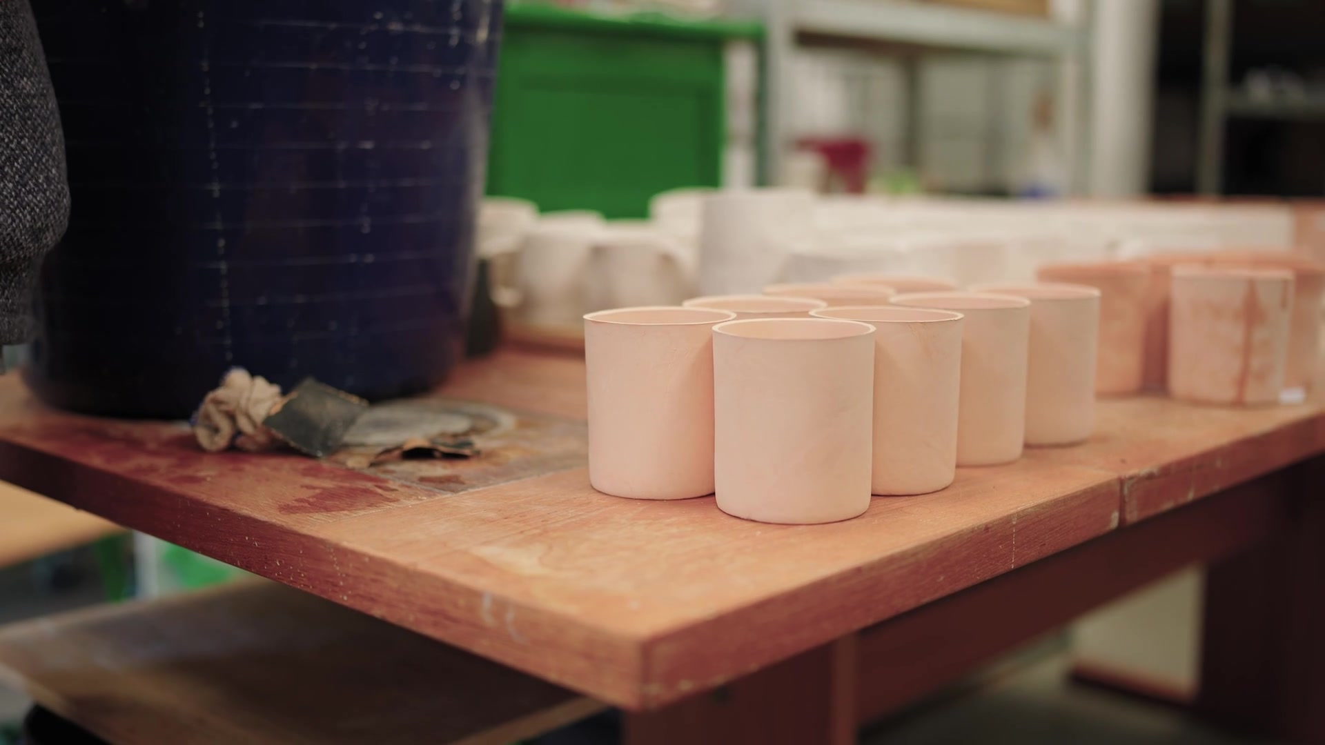 Pale ceramic cups cool on a pottery workshop table.