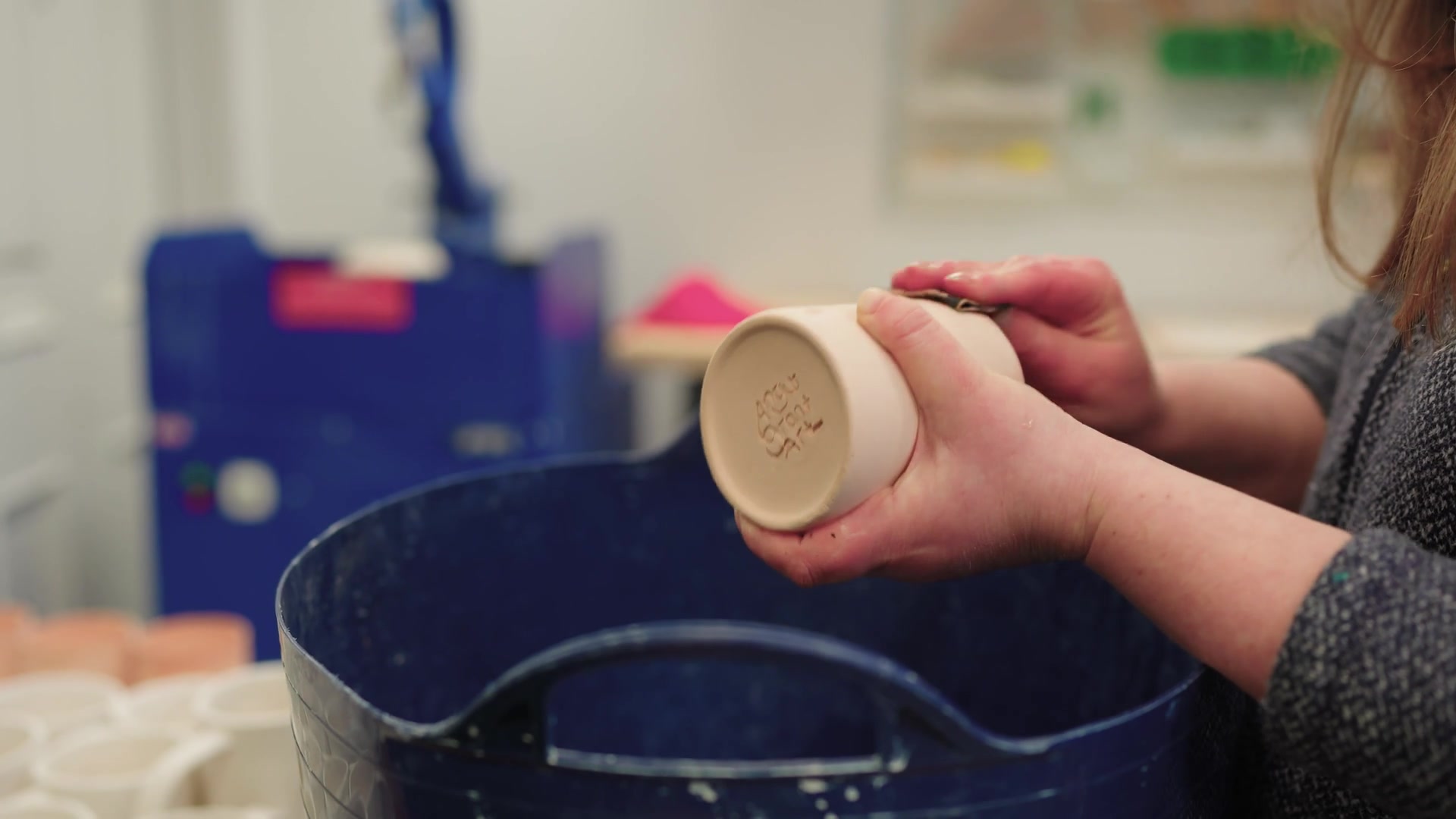 A potter's hands turn a mug upside down, the maker's stamp pressed into its base.