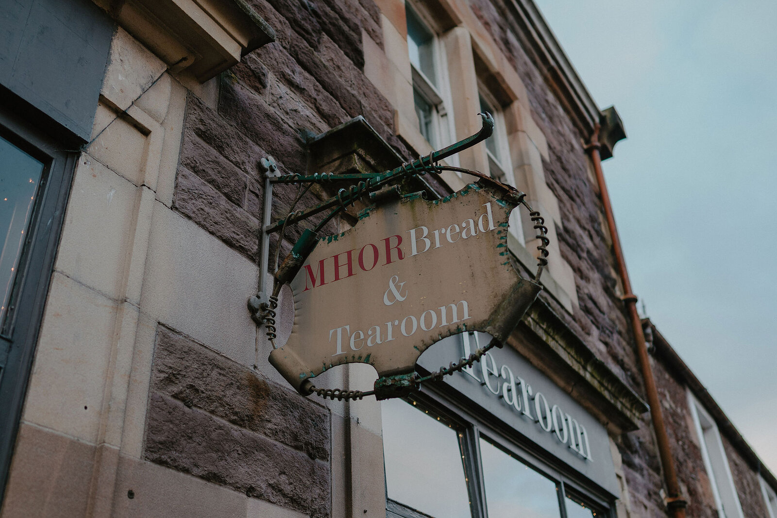 A hanging sign reading 'MHOR Bread & Tearoom' juts from a stone building above a shopfront lettered 'Tearoom'.