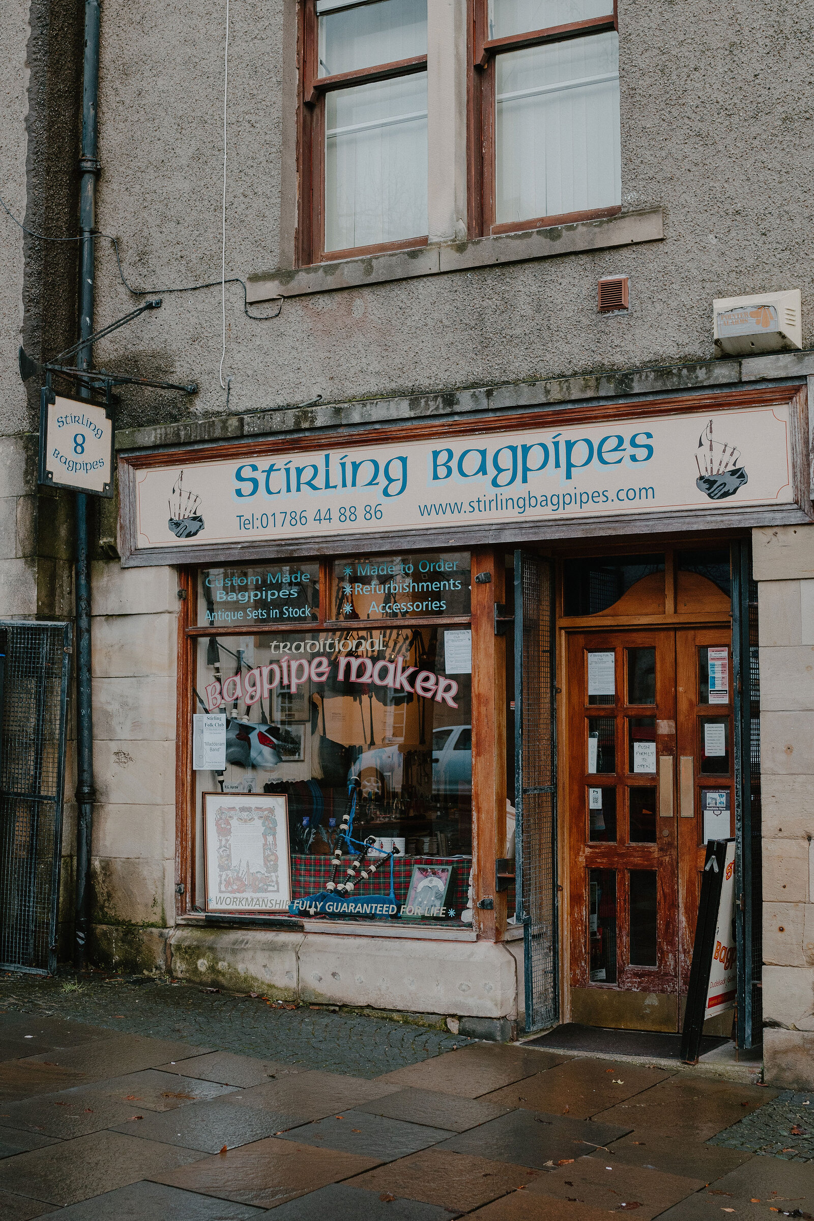 A shopfront carries a sign reading 'Stirling Bagpipes, Traditional Bagpipe Maker' above a window display of bagpipes and accessories.